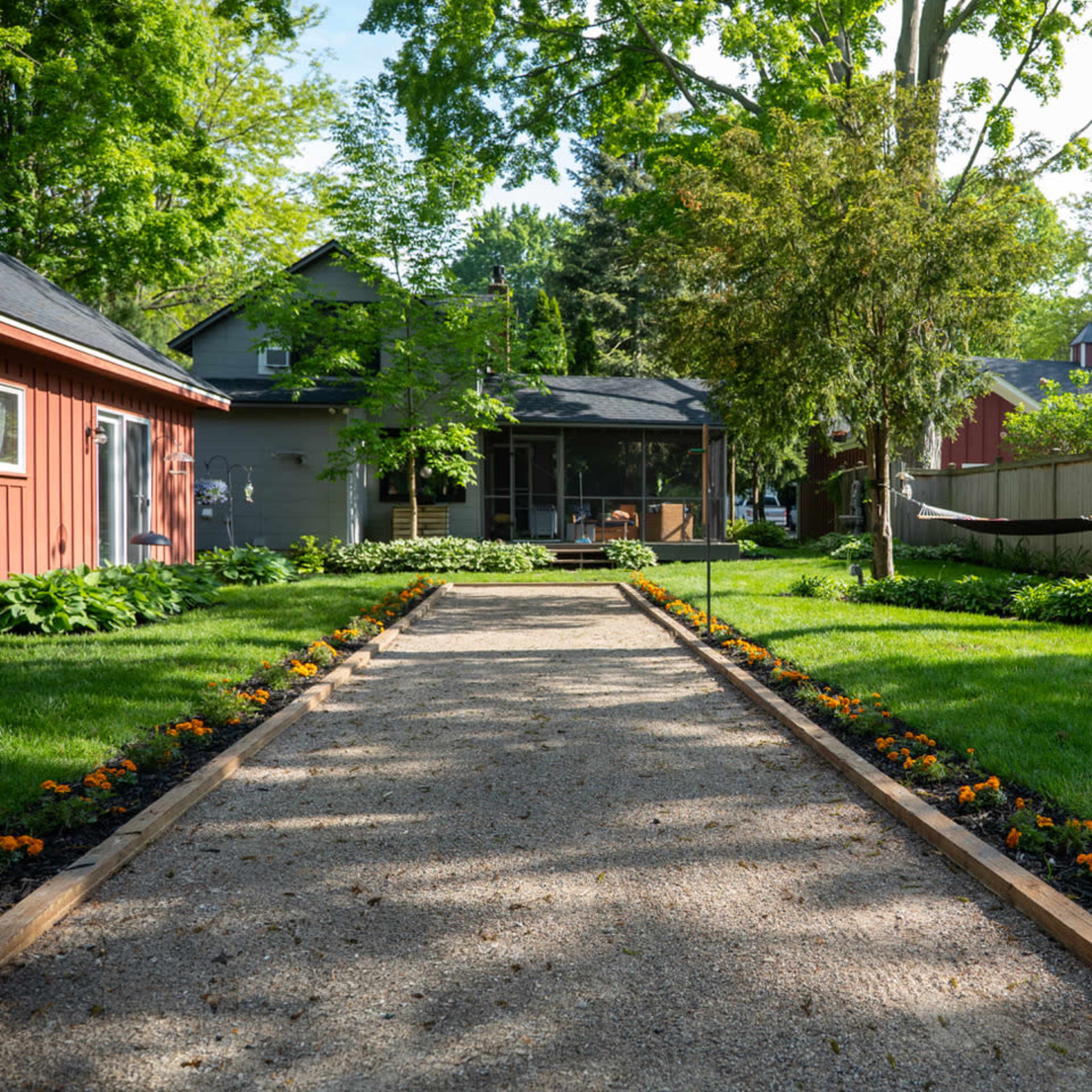 A gravel pathway lined with flowers leads to a house surrounded by greenery.