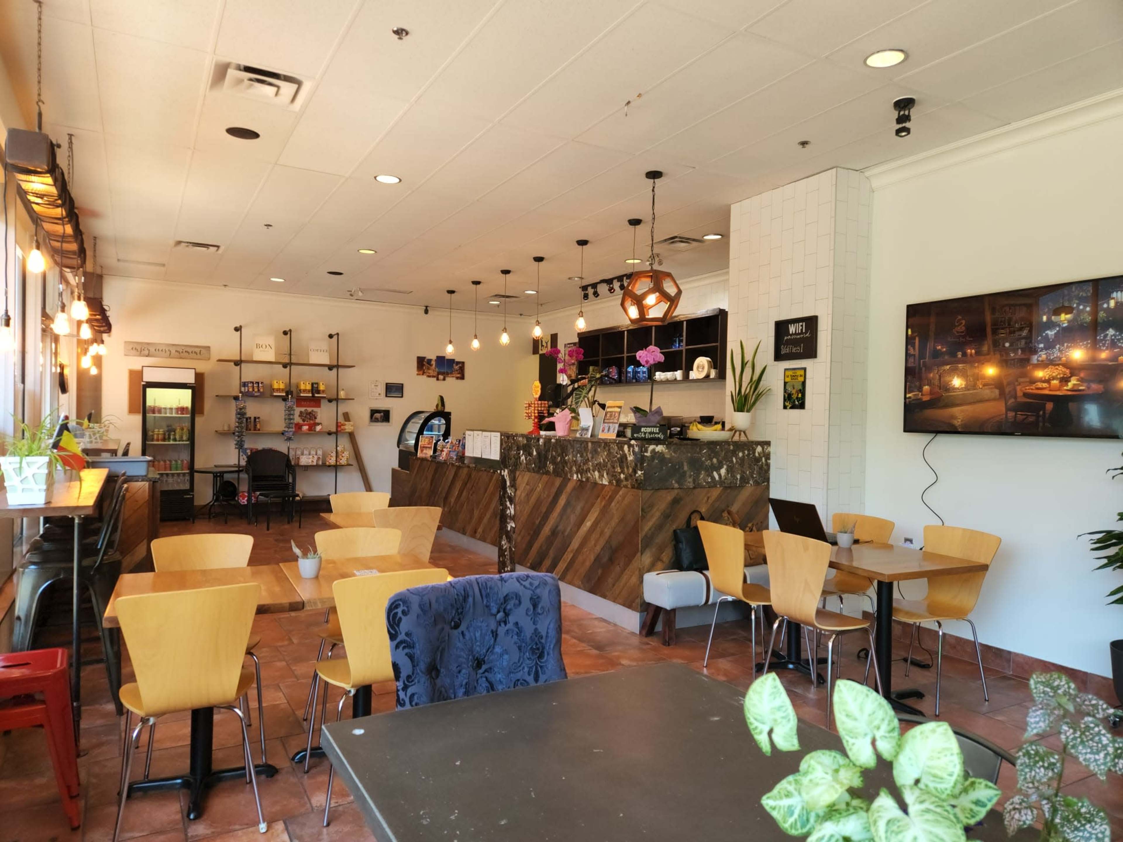 An interior of a café featuring a counter with a display, seating areas with wooden tables and chairs, and decorative lighting.