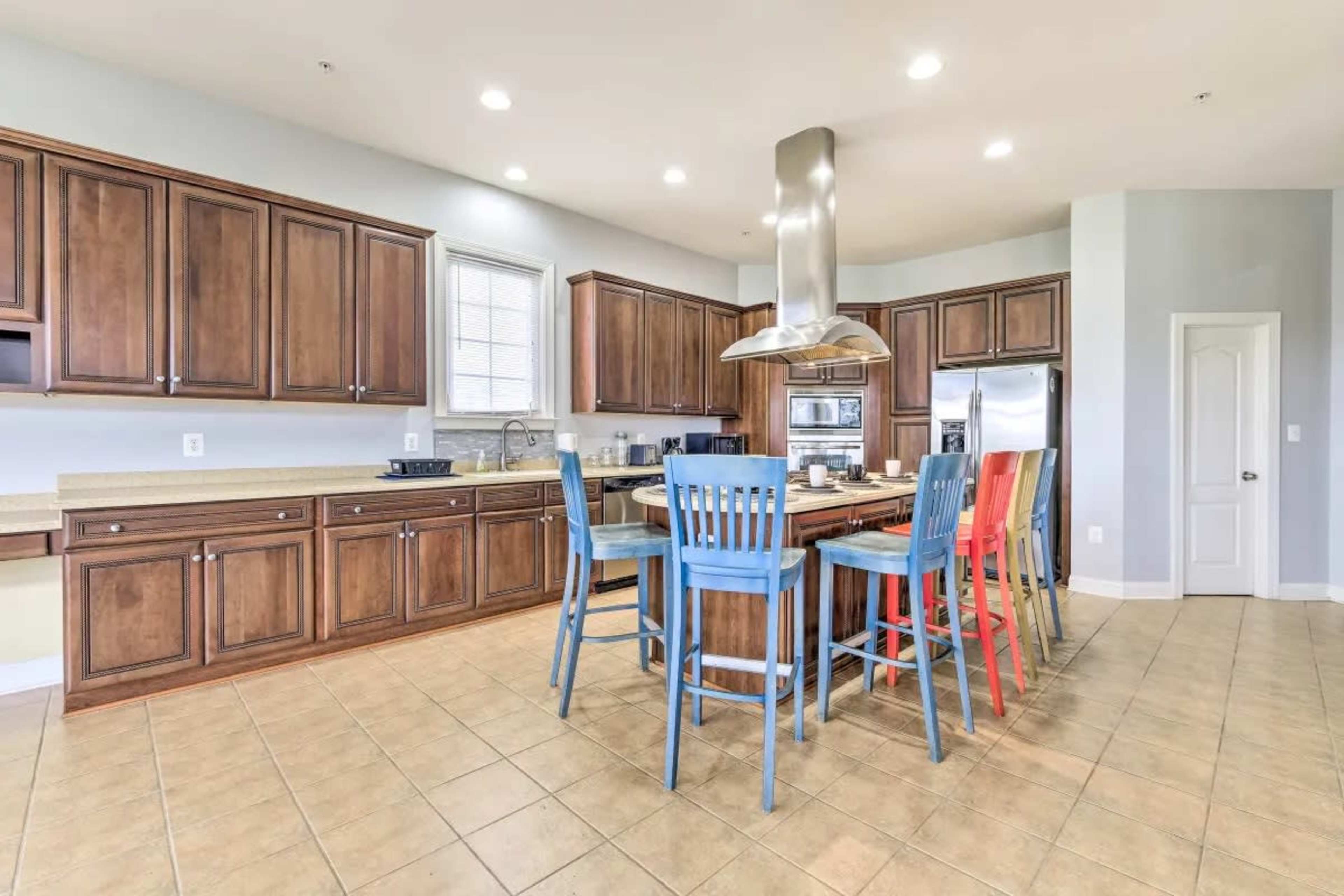 A spacious kitchen features wooden cabinets, a large island with colorful bar stools, and stainless steel appliances.