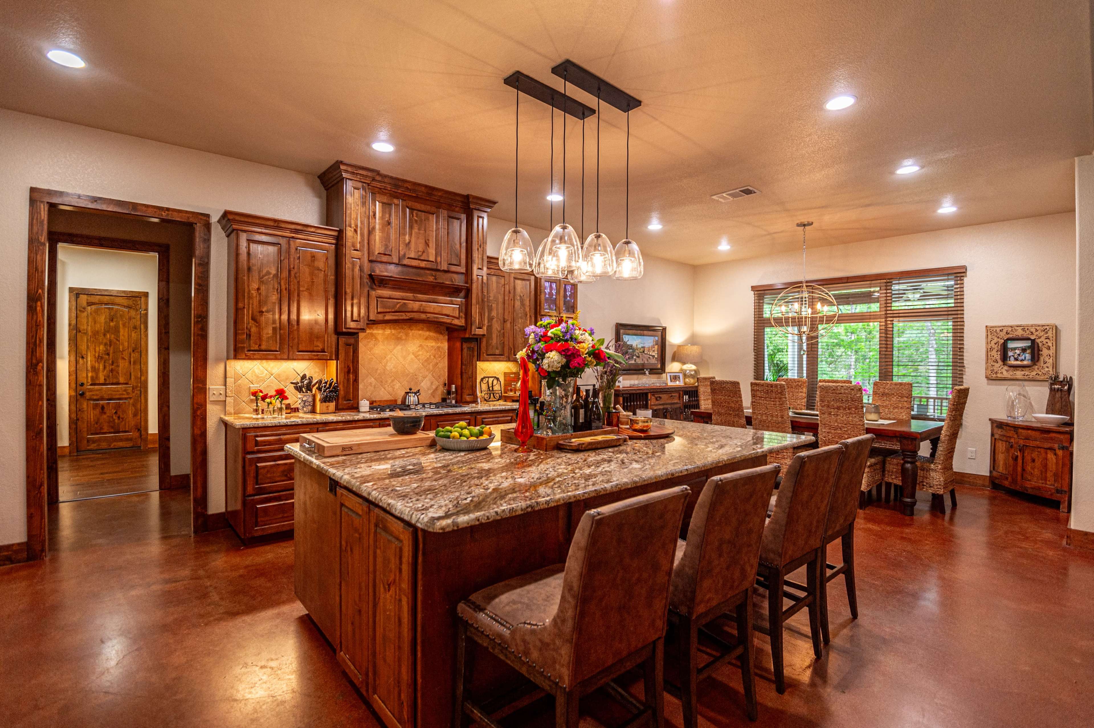 A spacious kitchen with wooden cabinetry, a large island with seating, and a dining area in the background featuring a wooden table and chairs.