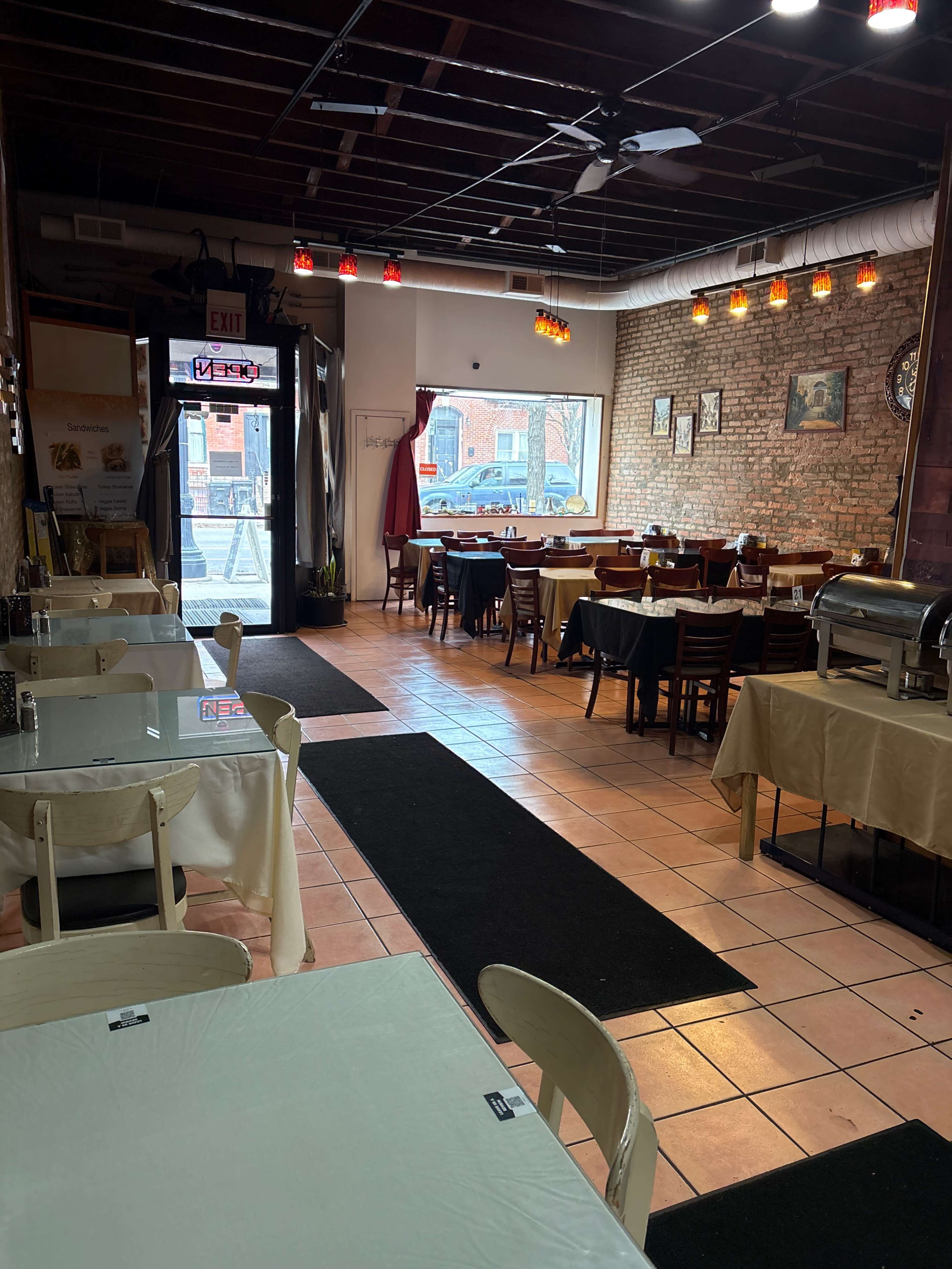 The image shows the interior of a restaurant featuring several tables, a buffet setup, and a doorway leading outside.