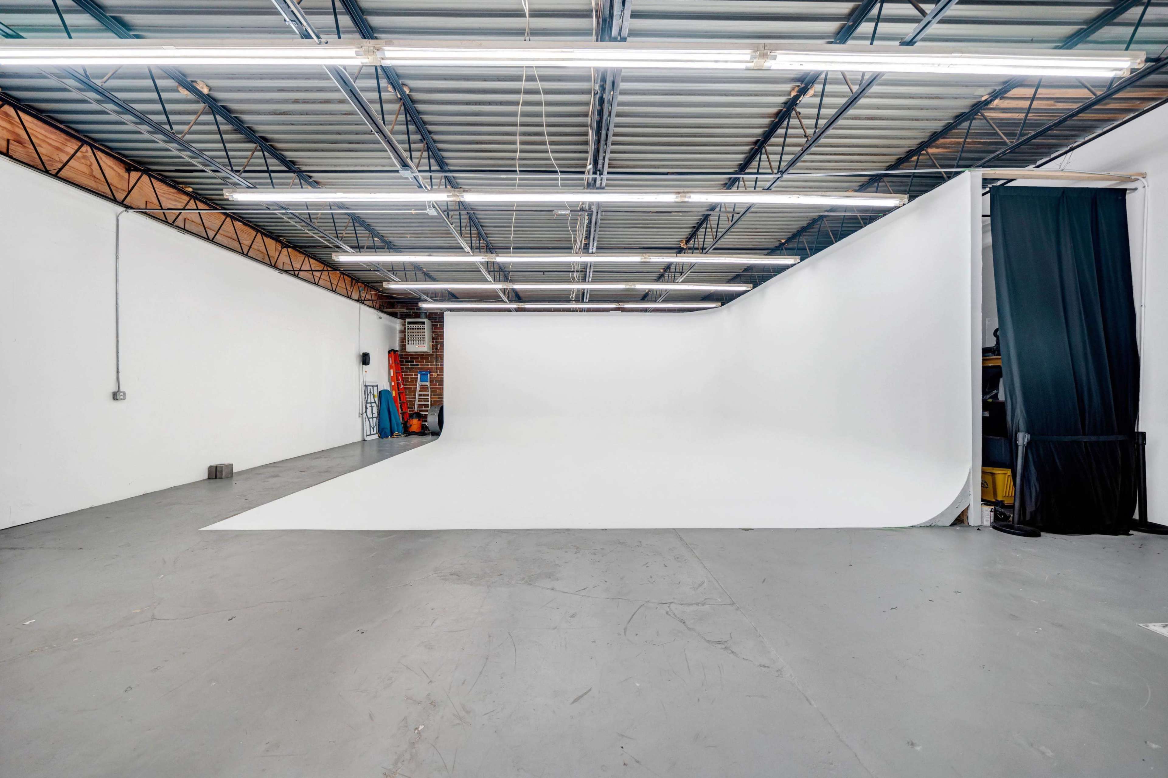 A spacious studio with a seamless white backdrop, concrete floor, and overhead lighting in a well-lit environment.