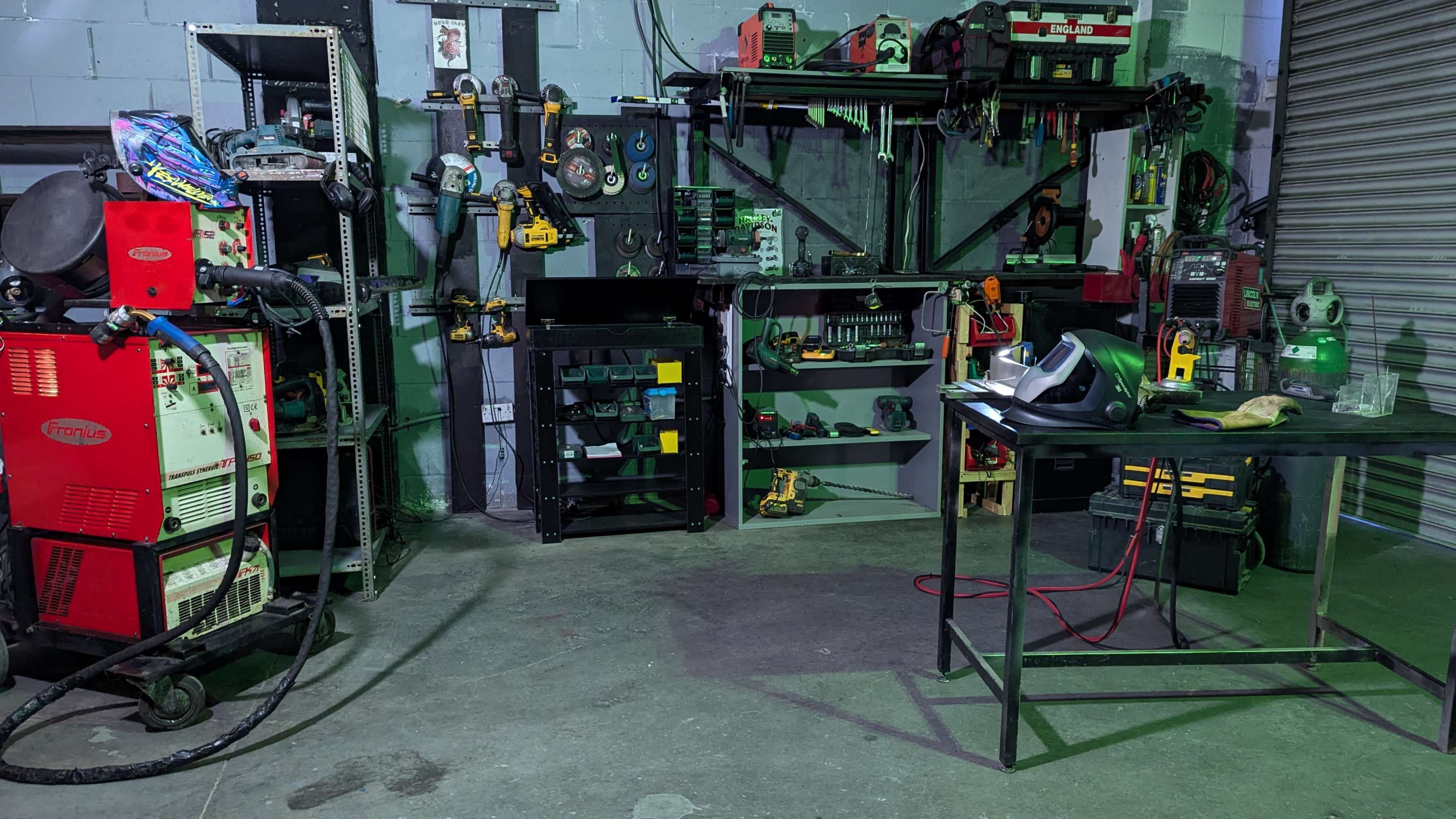 The image shows a workshop with various tools and equipment organized on shelves, including a welding machine, power tools, and storage units, in a well-lit industrial setting.