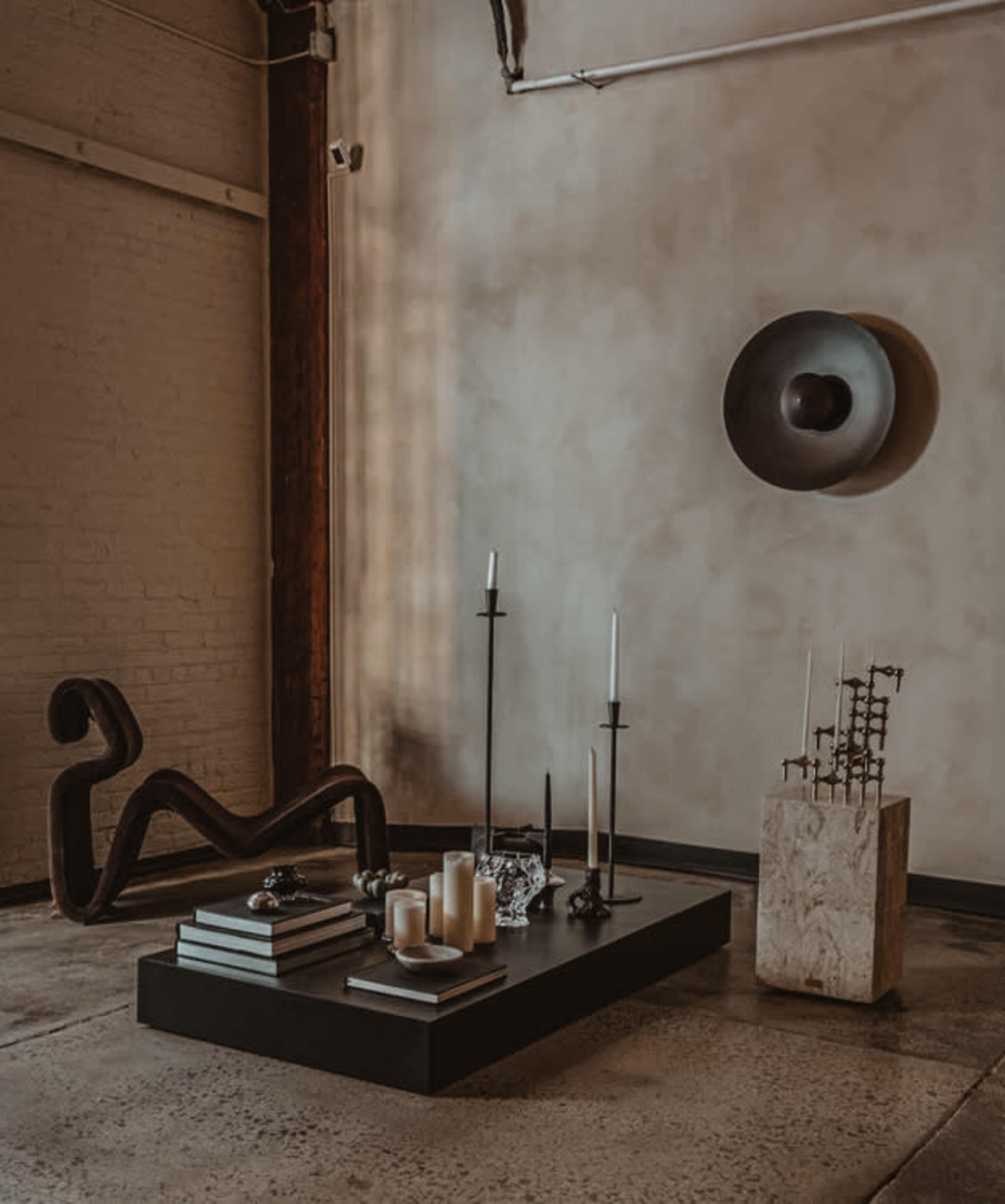 A minimalist interior features a low coffee table with books and candles, accented by various sculptures and wall art.