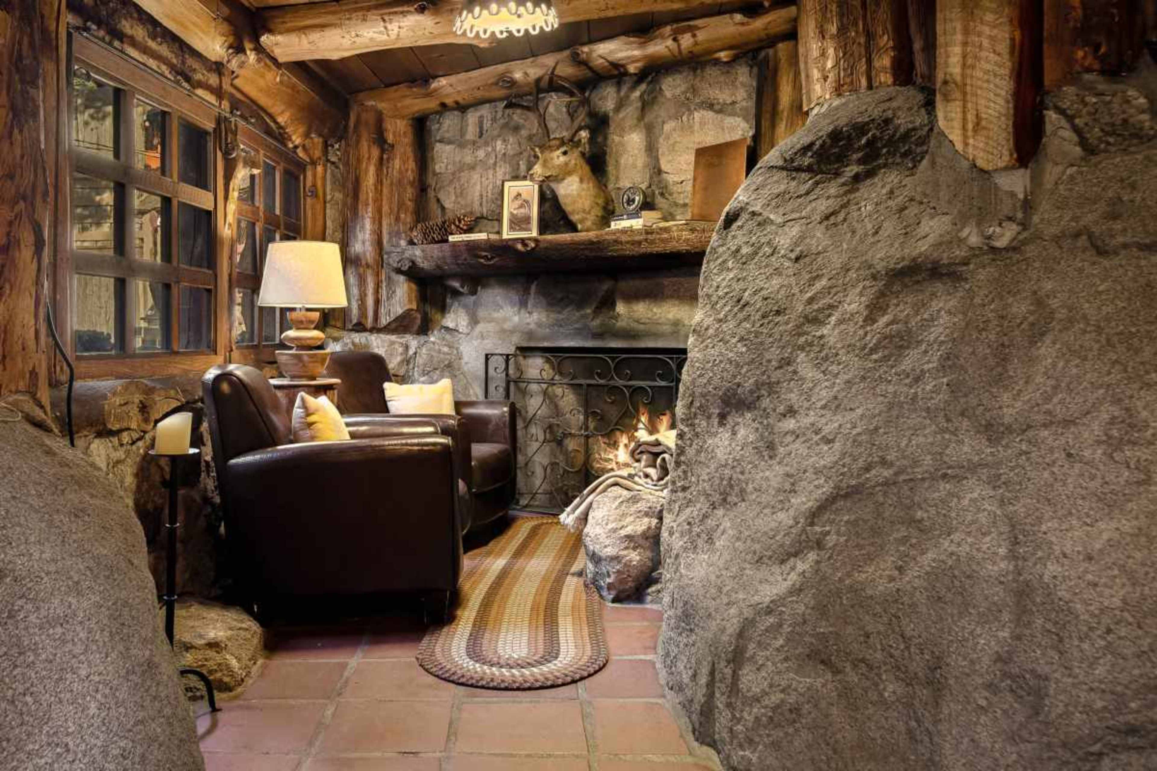 A cozy seating area features a brown leather chair near a stone fireplace with a rustic log mantel and a lamp beside it.