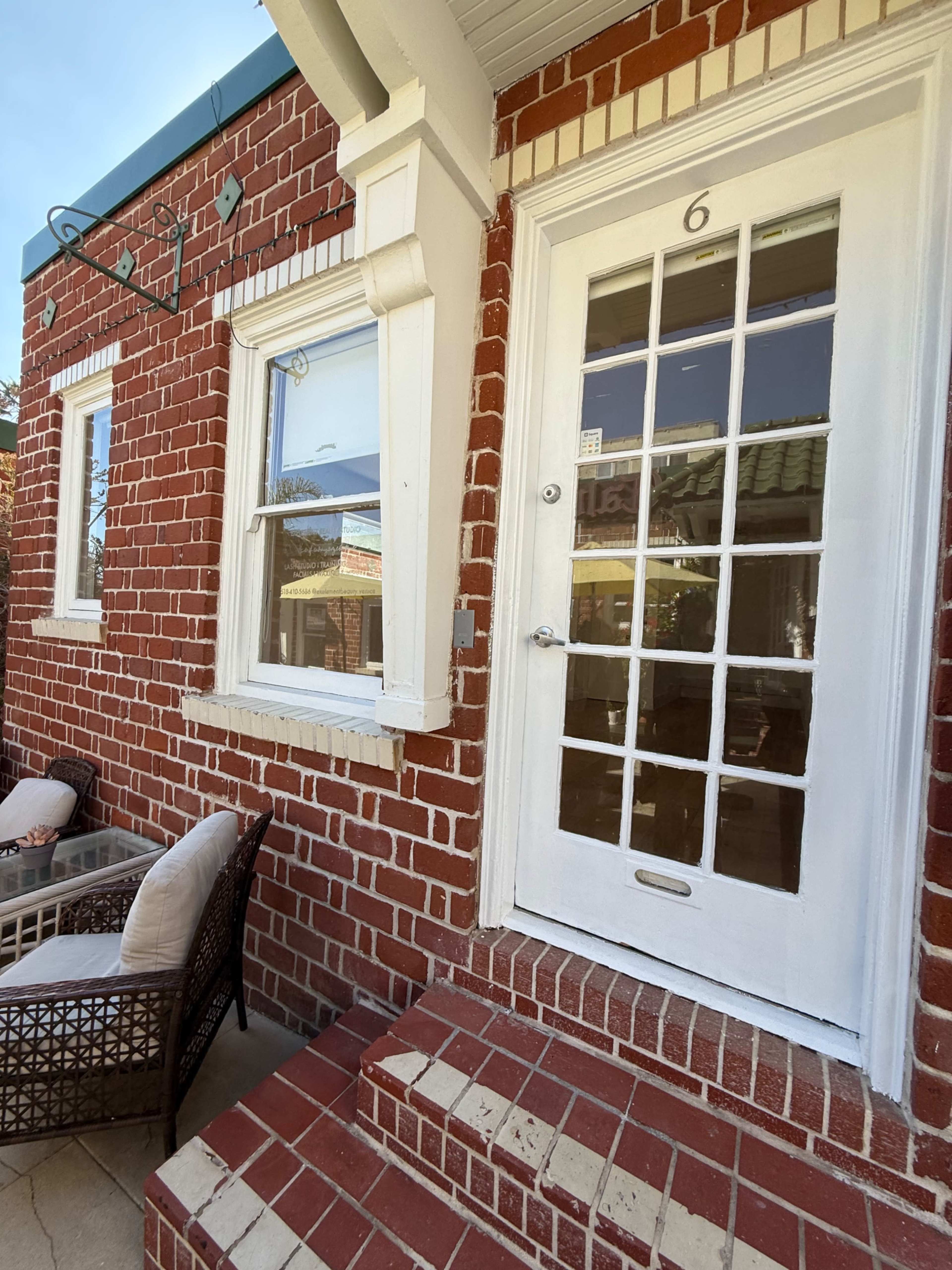 The image shows a brick exterior of a building with a white door featuring glass panes and a small stoop with brick steps.