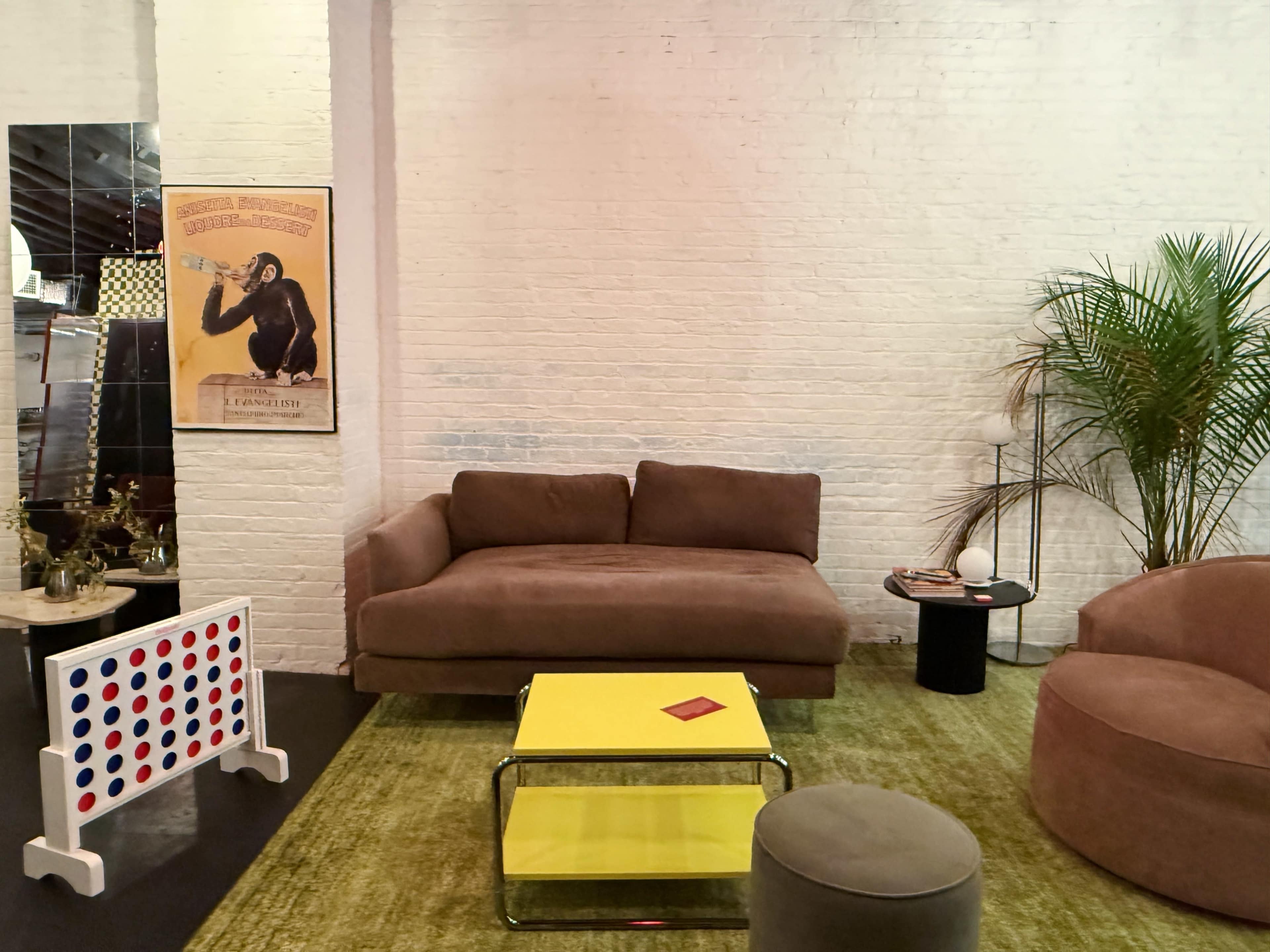 The image shows a modern living area featuring a brown sofa, a yellow coffee table, and a green area rug, with a decorative poster on the wall and a potted plant in the corner.