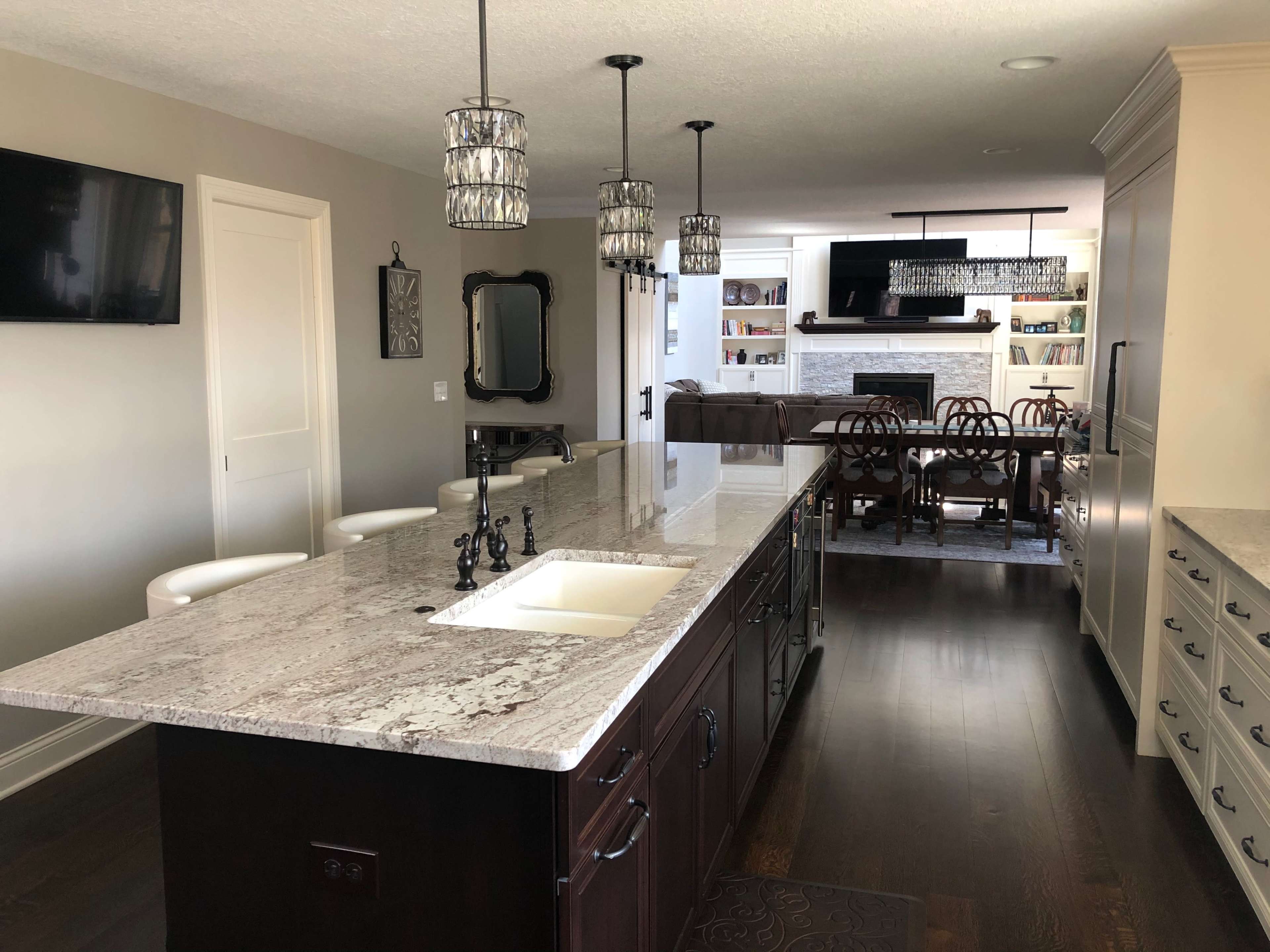 A modern kitchen with a large granite island, sleek cabinetry, and a view of a living room area in the background.
