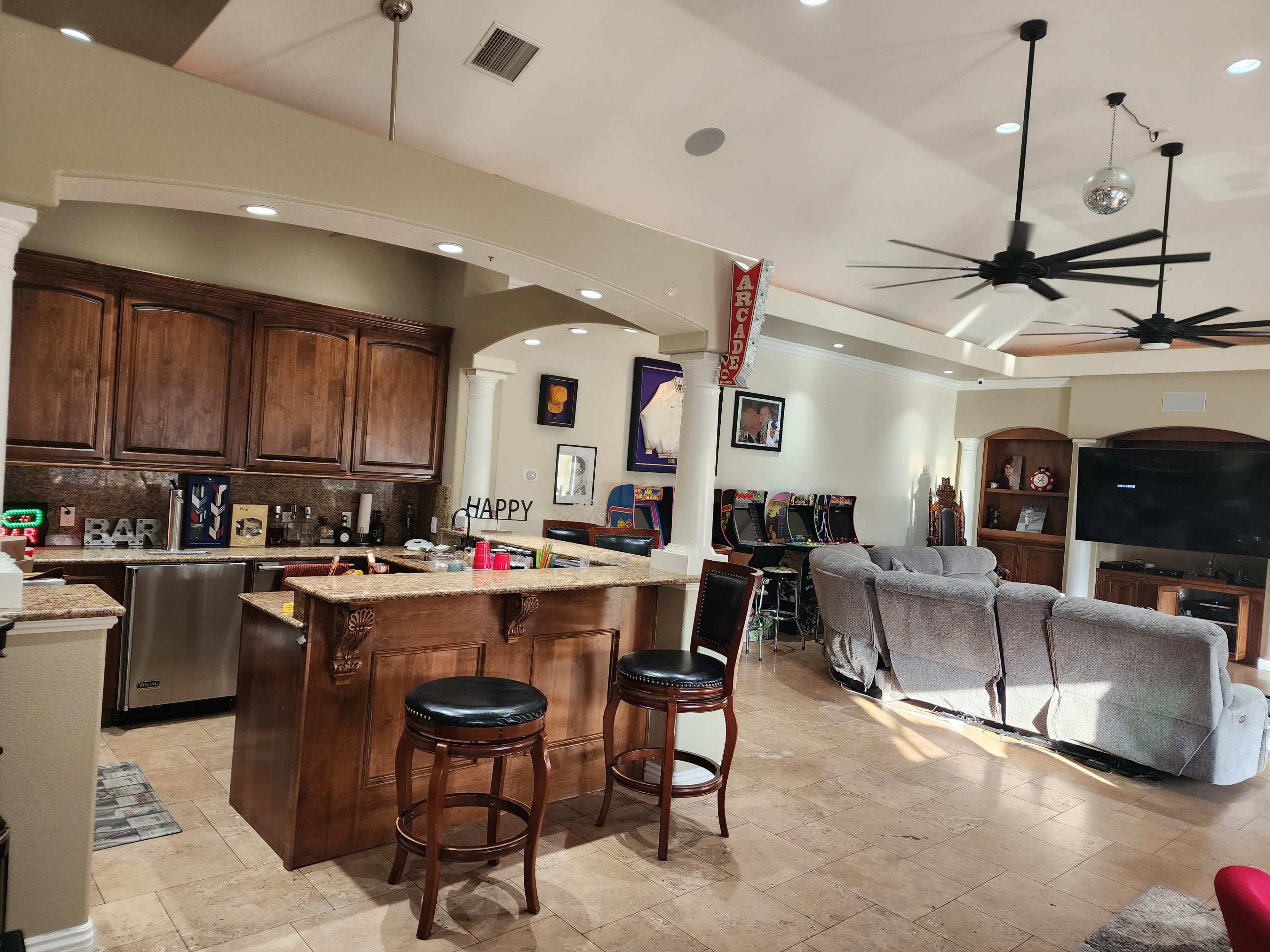 A spacious open-concept kitchen and living area featuring a bar counter with stools, wooden cabinetry, and a seating area with gray sofas.