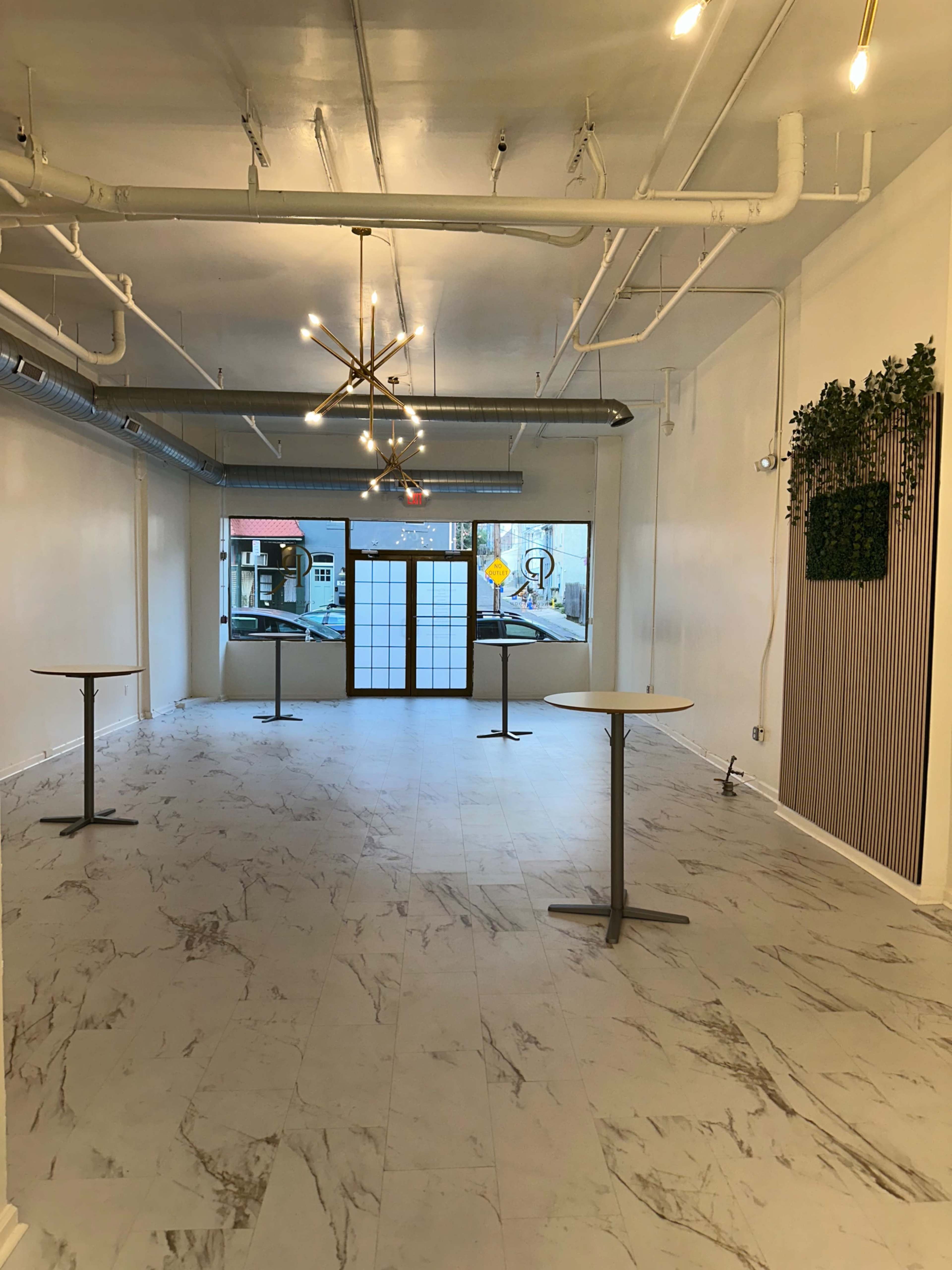 The image shows an empty indoor commercial space with light-colored walls, marble-patterned flooring, and several round tables positioned throughout.
