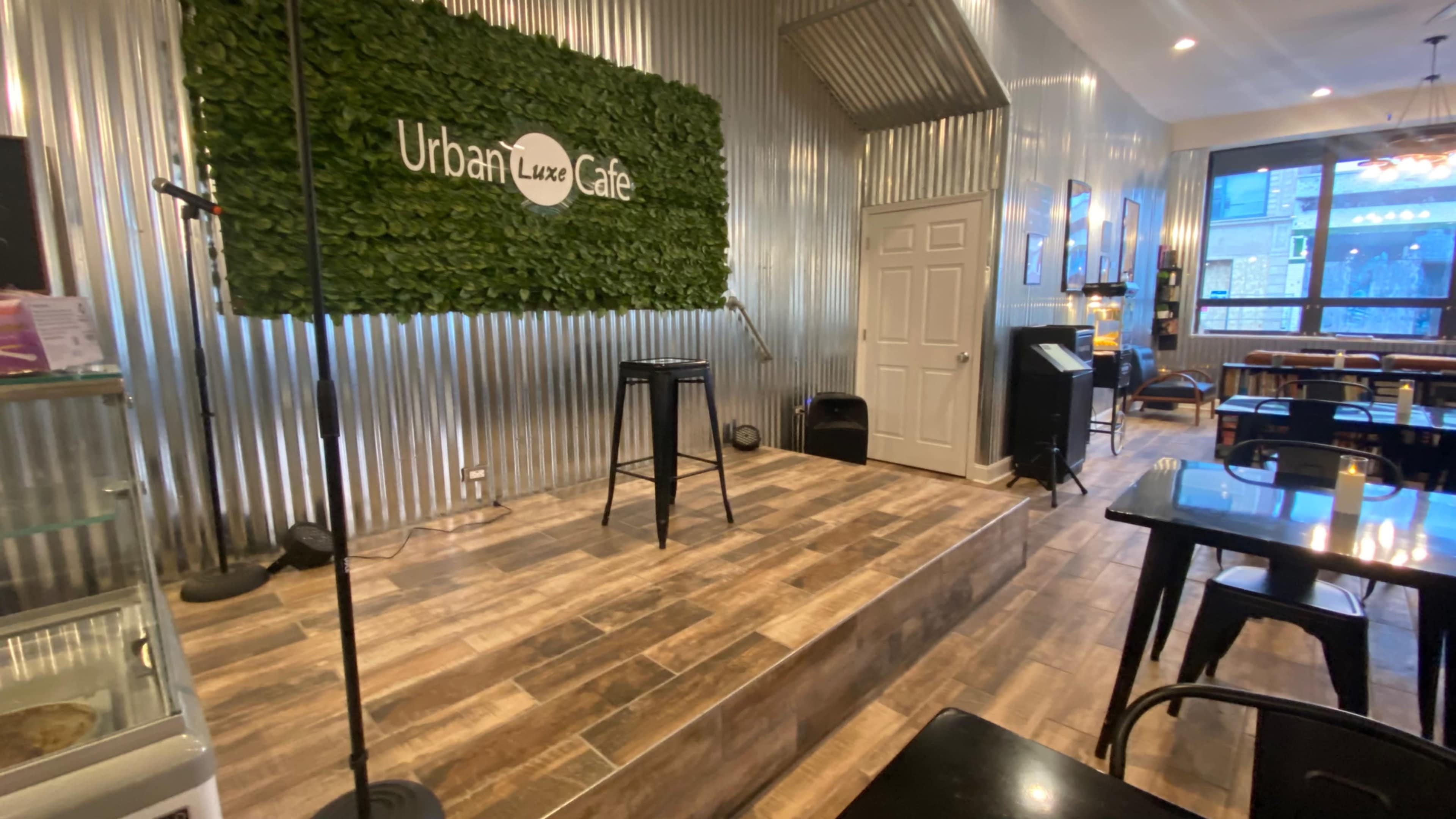 The interior of Urban Luxe Café featuring a small stage with a microphone setup, surrounded by metal and wooden decor.