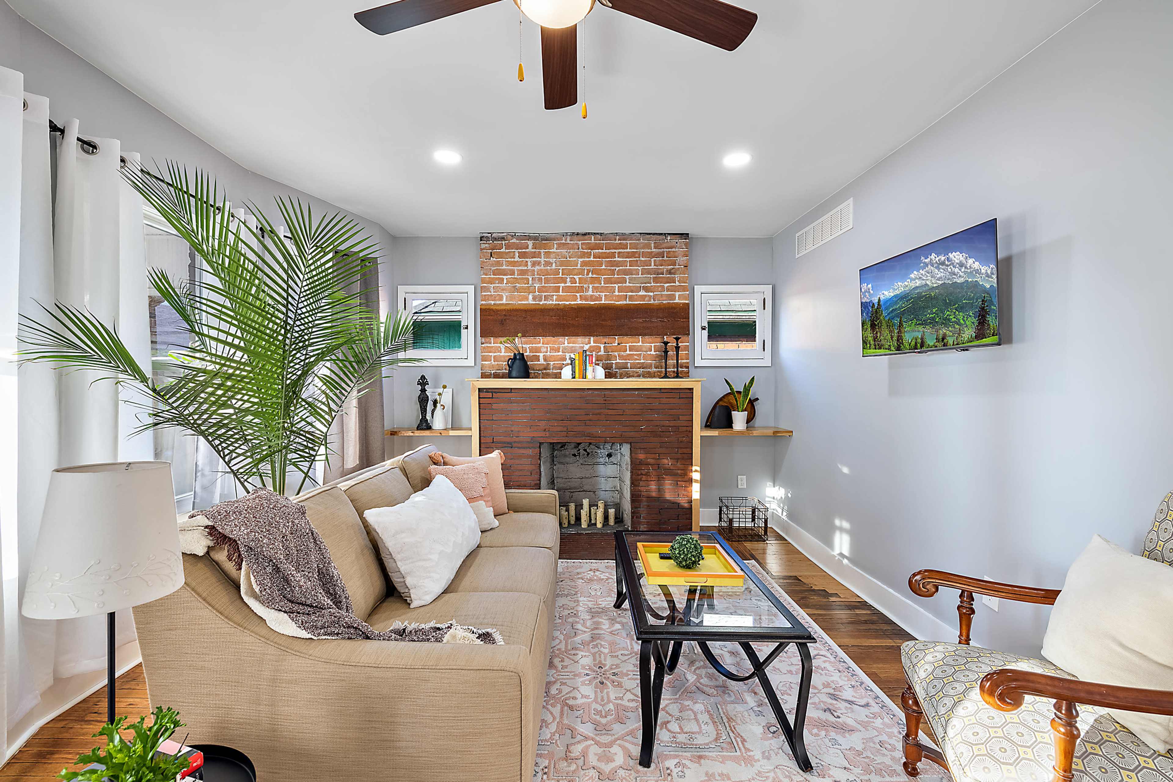 A cozy living room features a brick fireplace, a sofa, and a television mounted on the wall.