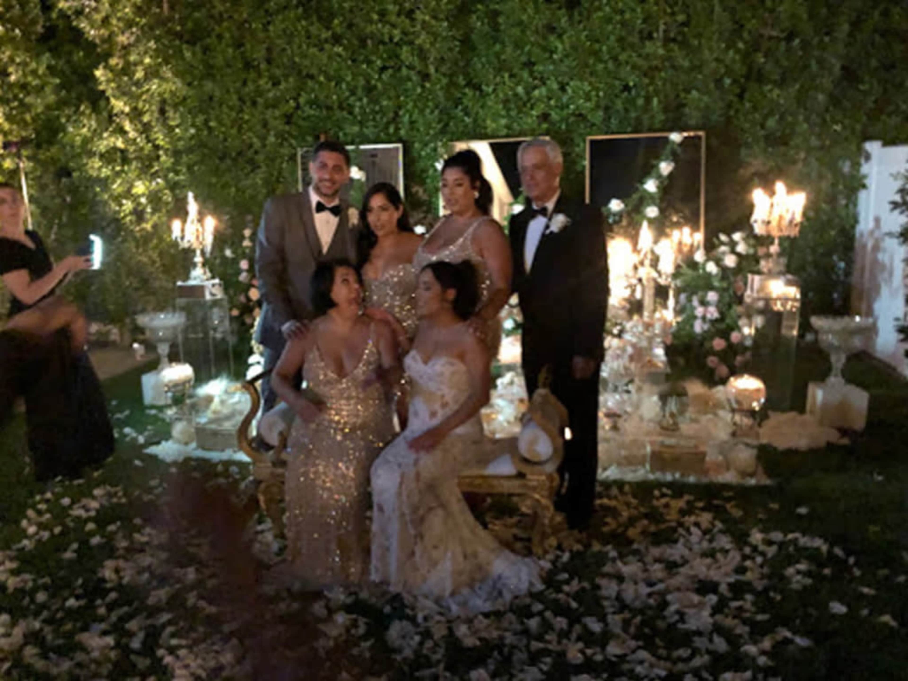 A group of six people poses for a photo in front of elegant decorations, including candles and floral arrangements, at an outdoor event.