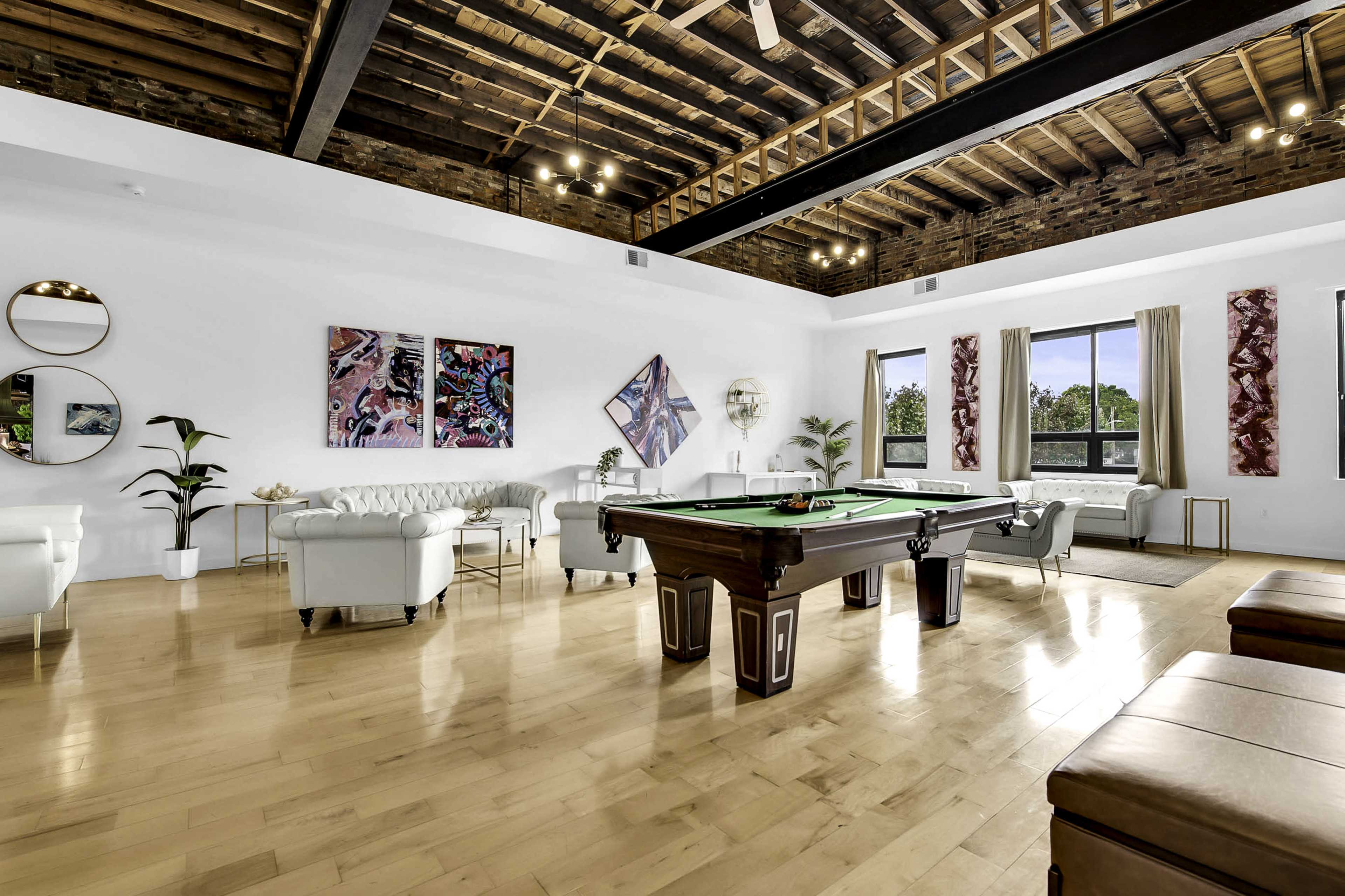 A spacious game room featuring a pool table, modern seating arrangements, and large windows with views of the outdoors.