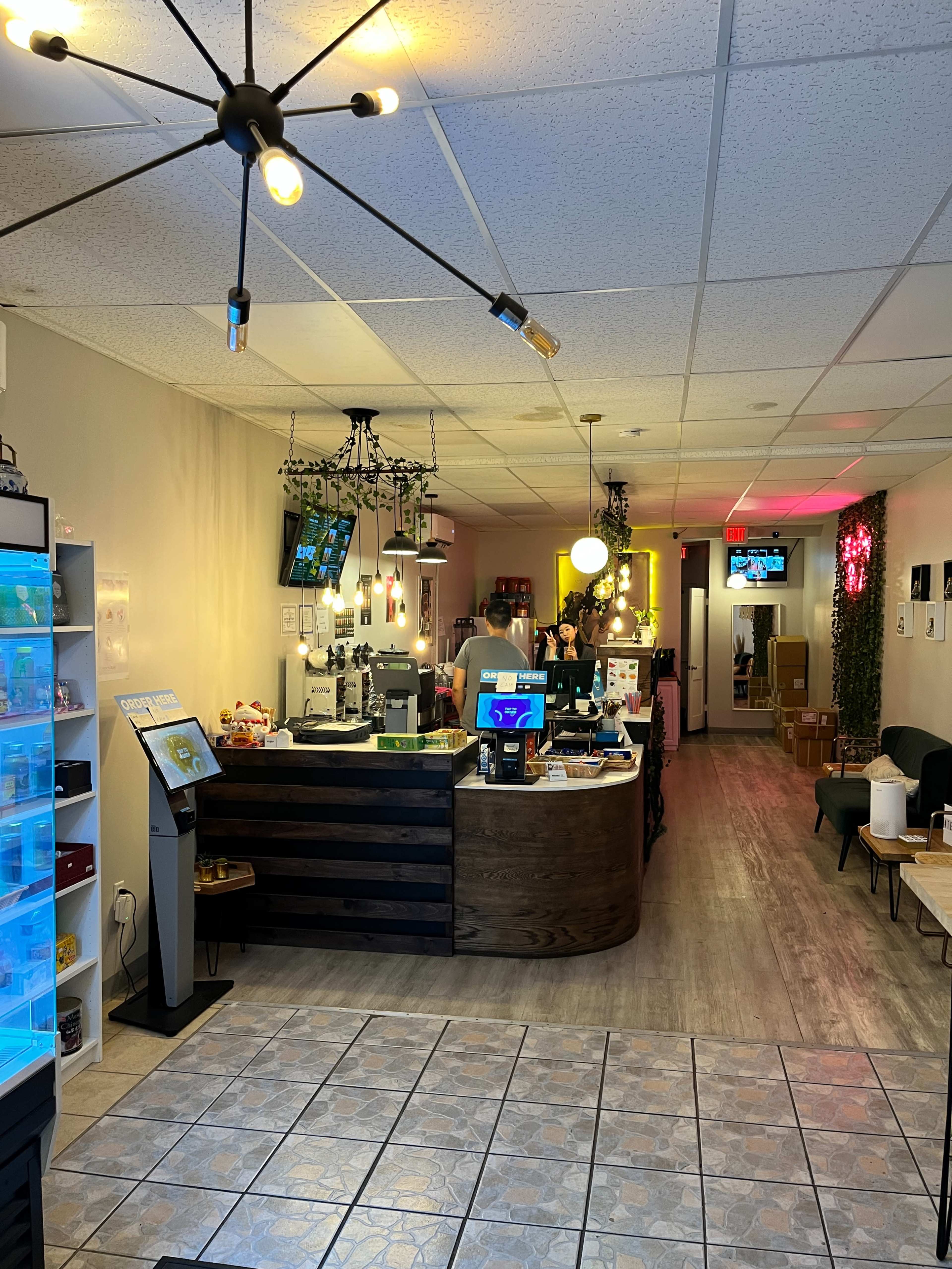The interior of a modern café, featuring a service counter with a cash register and a variety of displays, while tables and seating are arranged in a spacious layout.