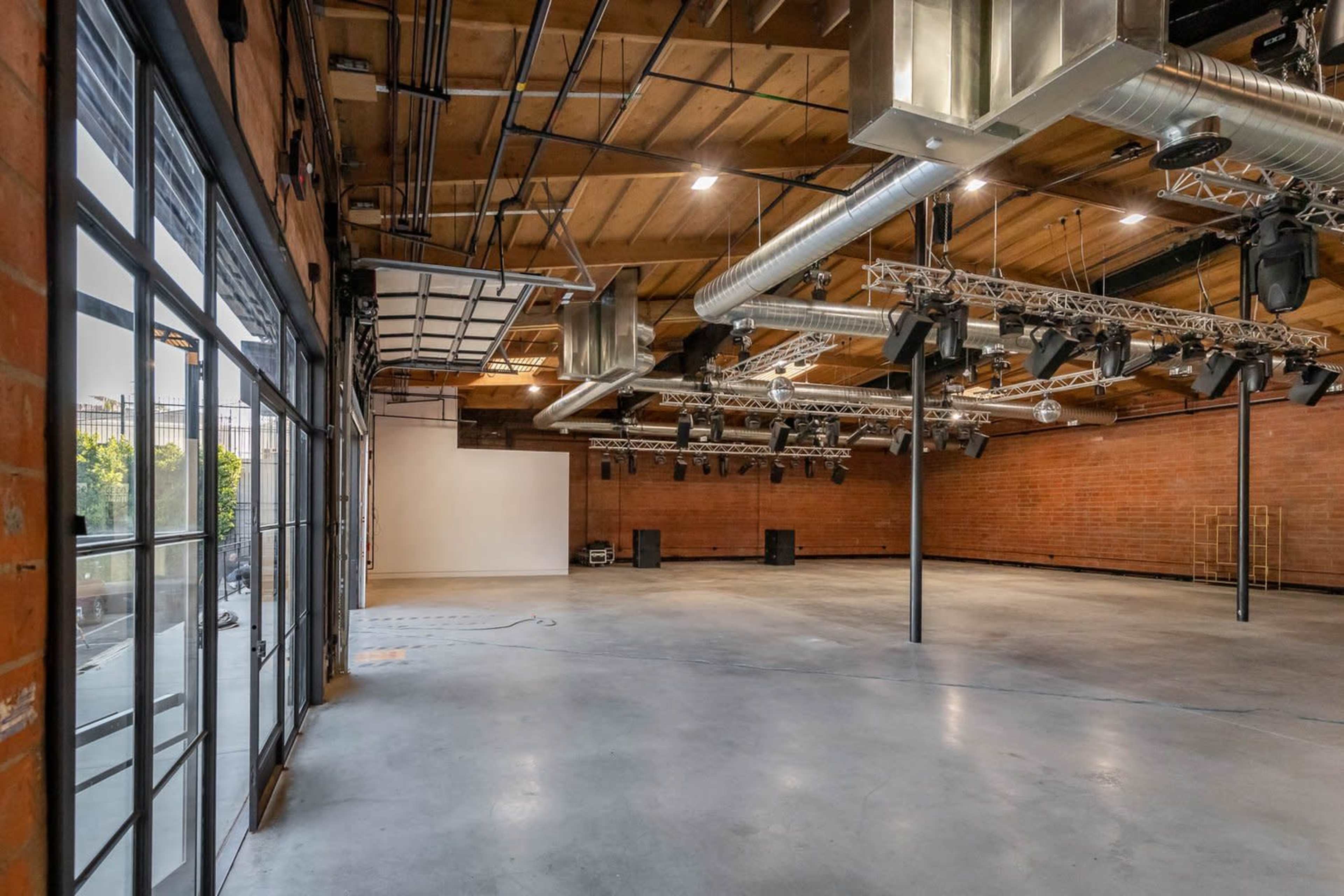 A spacious event venue with exposed wooden beams, industrial lighting fixtures, and brick walls, featuring an open area for performances or gatherings.