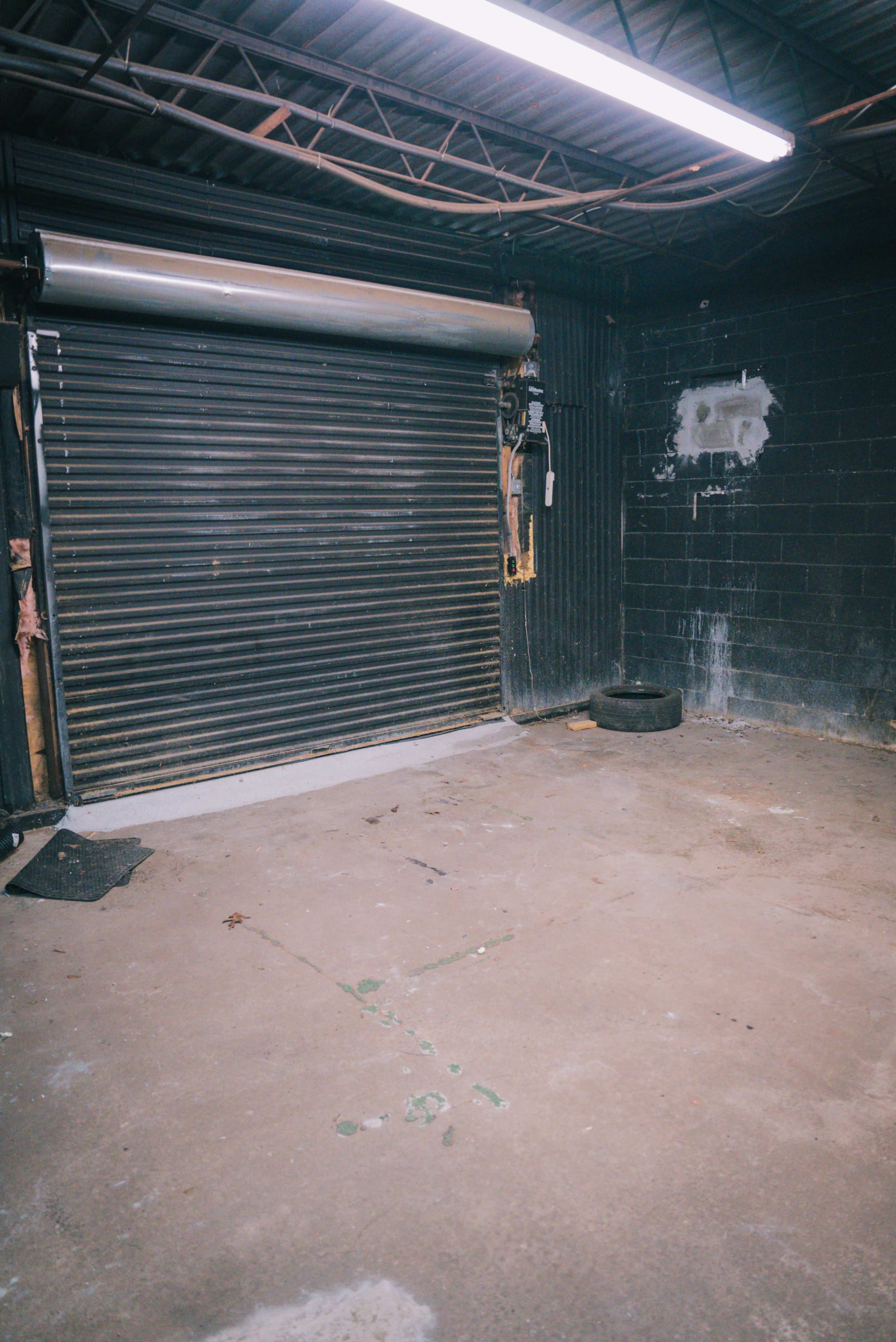 The image shows an empty industrial space with a closed metal roll-up door, a tire, and a concrete floor.