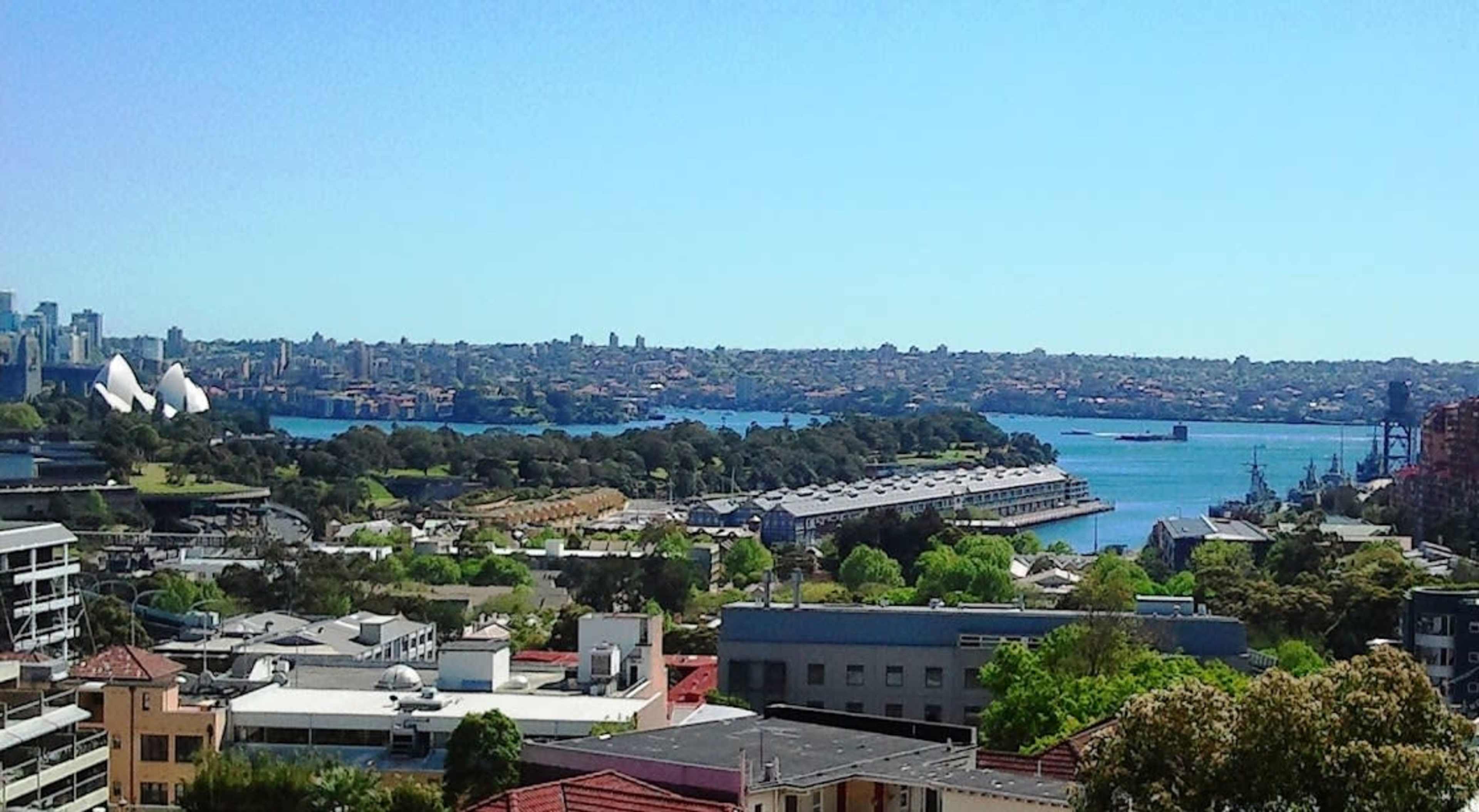 A panoramic view of Sydney's waterfront, featuring the Opera House and various buildings lined along the water's edge.