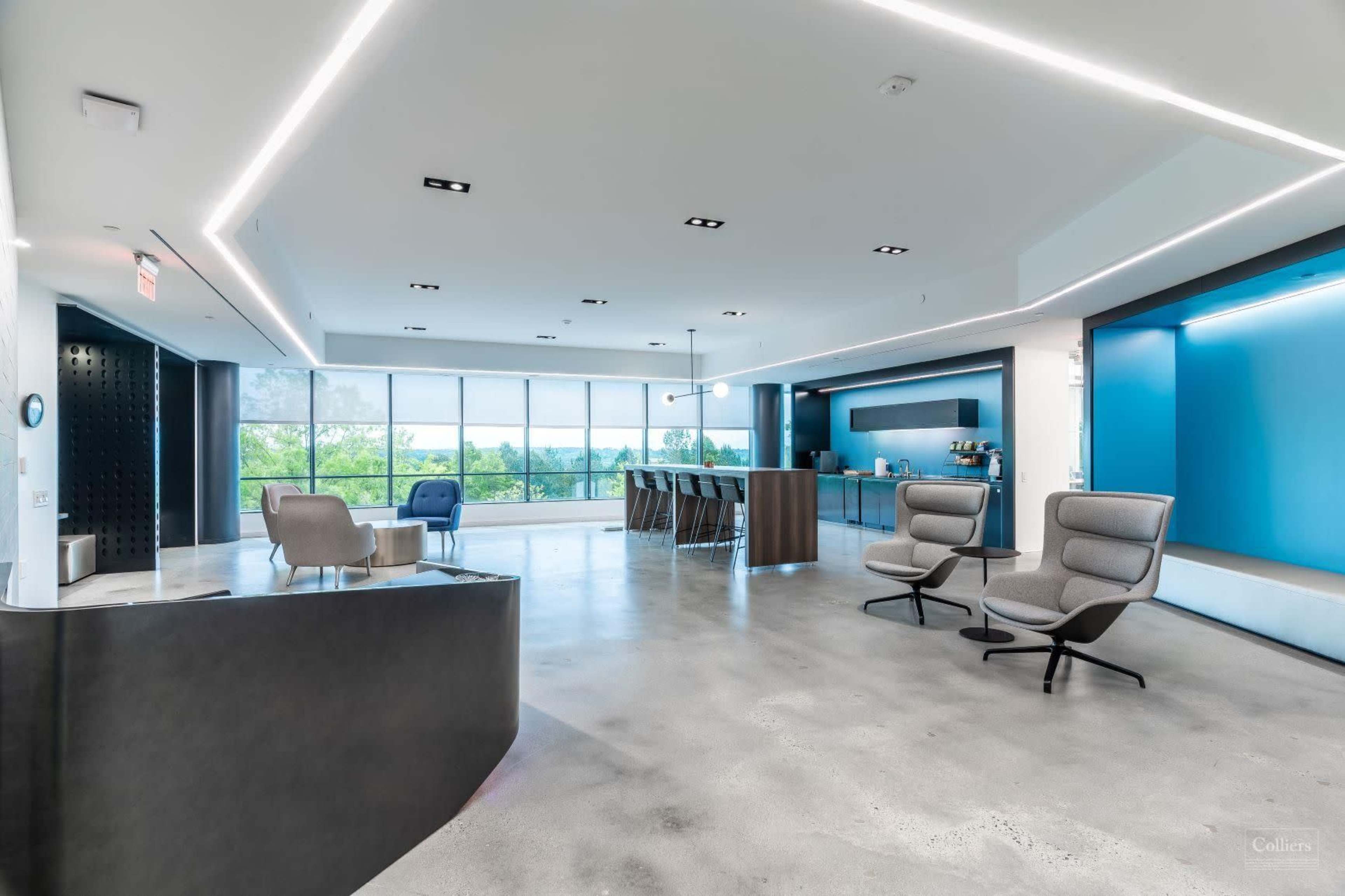 A modern office interior features sleek furniture, large windows, and an open layout with a bar area.