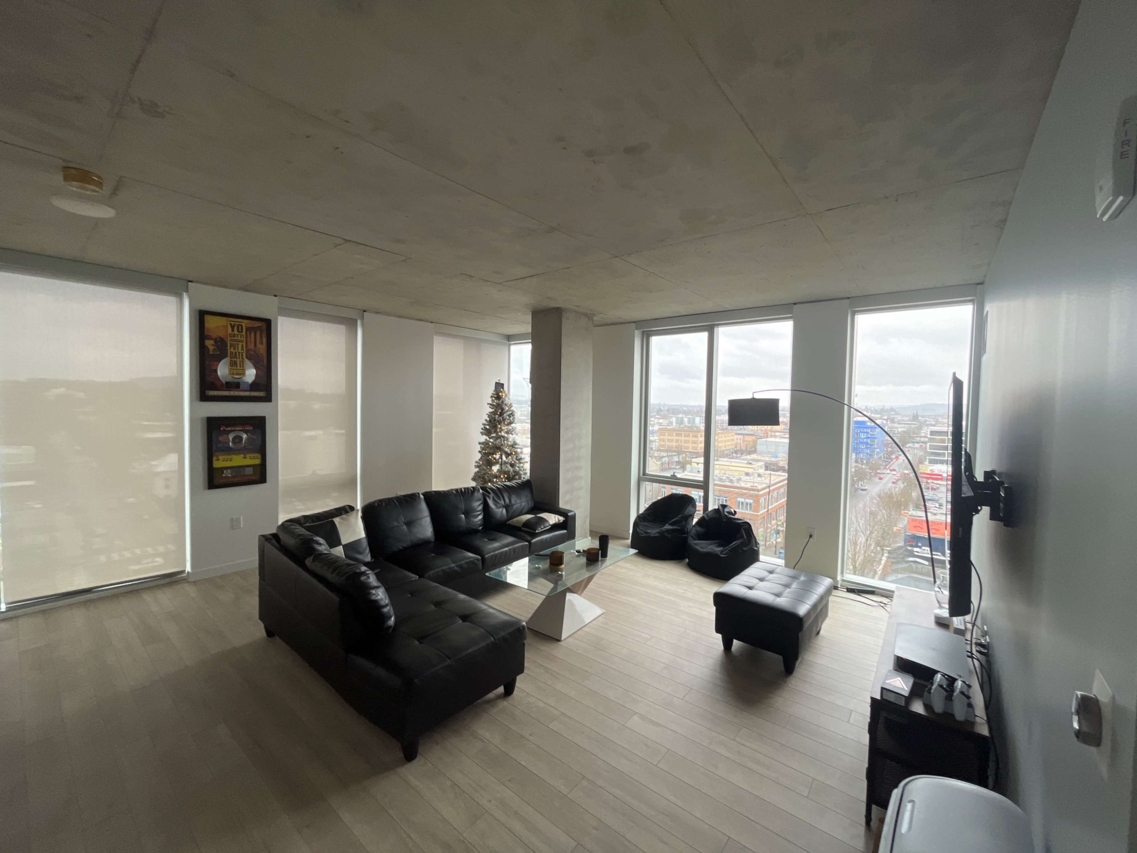 A modern living room with a black sectional sofa, a glass coffee table, and large windows providing a view of the city skyline.