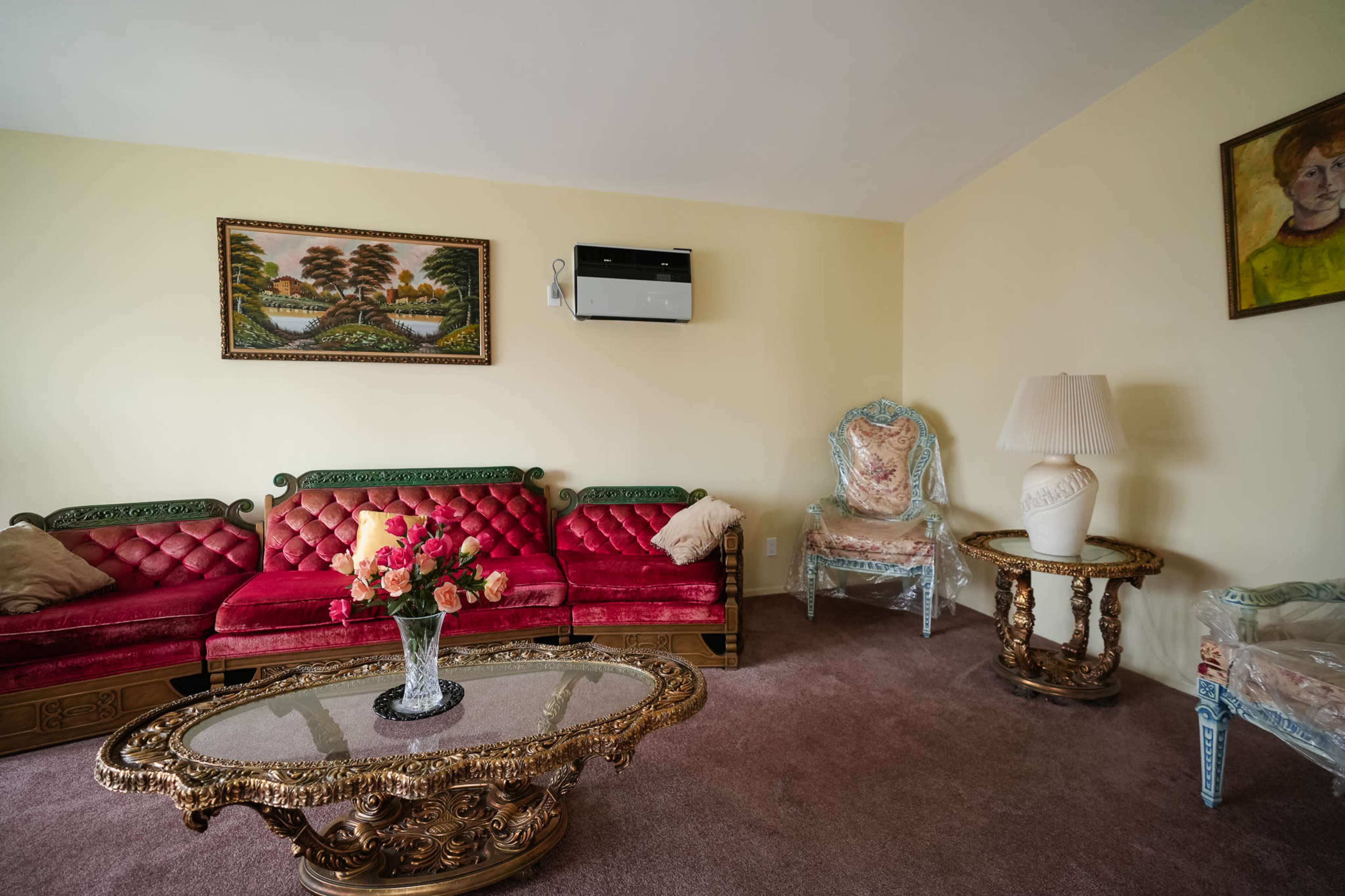 The living room features a red upholstered sofa set around an ornate glass coffee table, with a floral centerpiece and a painting on the wall.