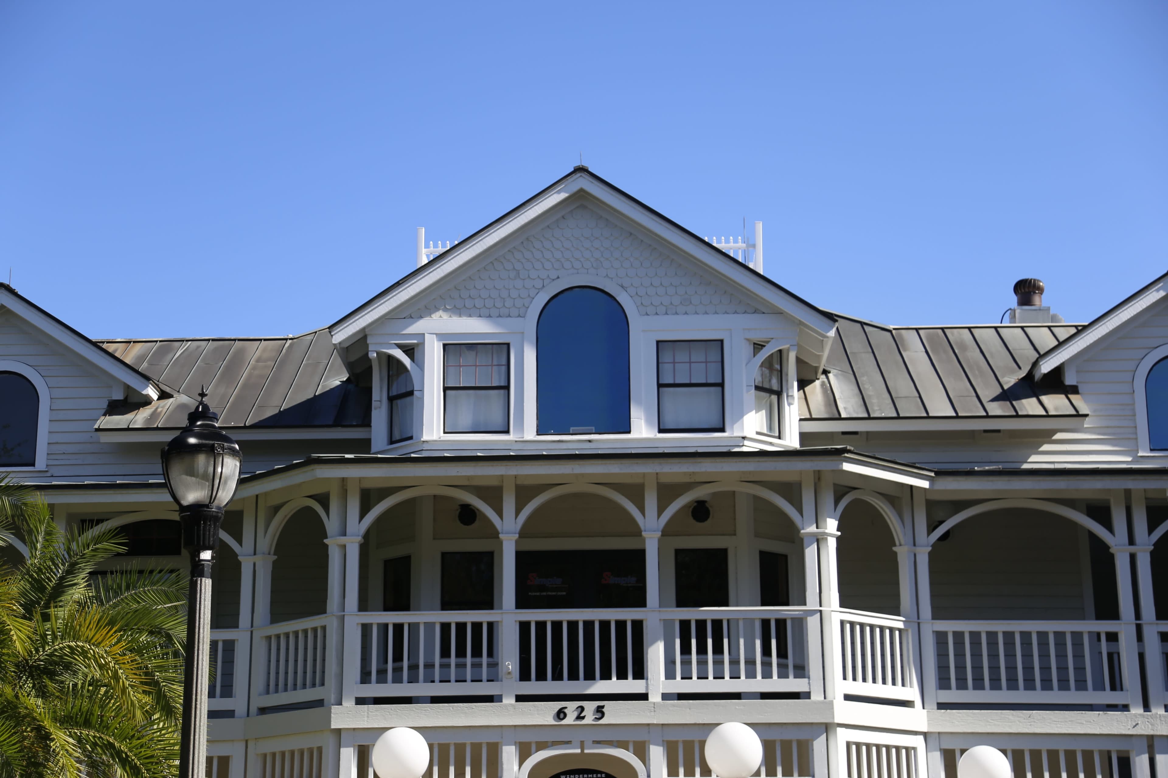 The image shows a multi-story building with a peaked roof, white railings, and large windows under a clear blue sky.