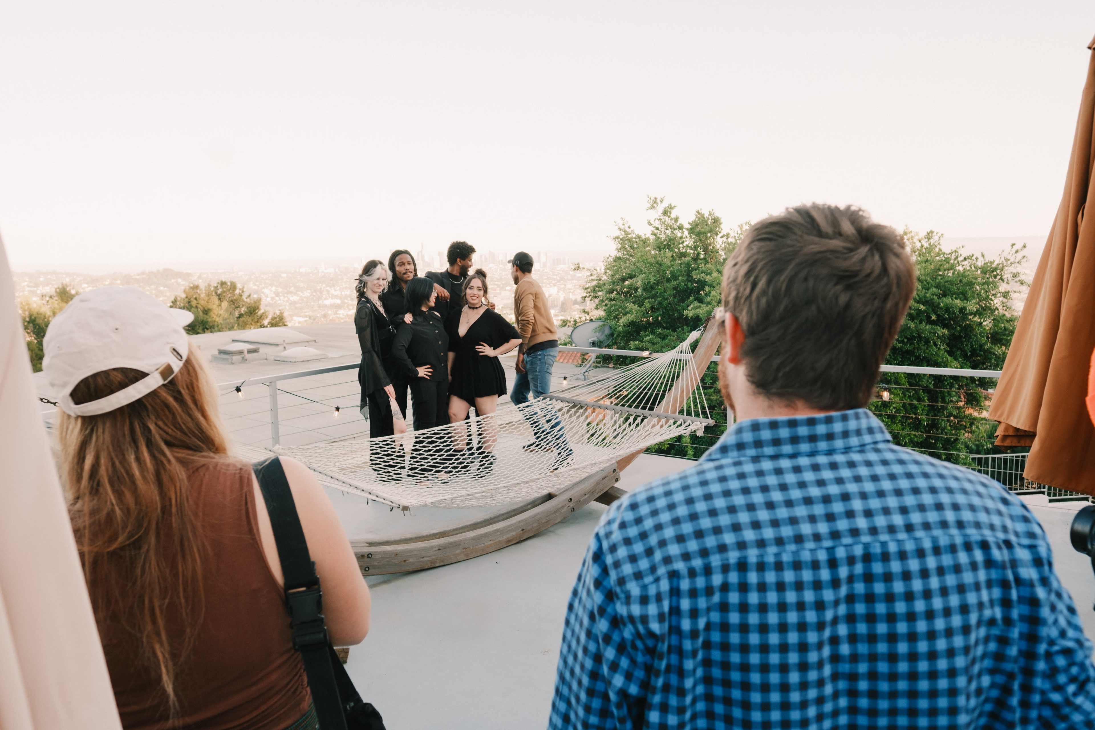 A group of people poses for a photo on a hammock while others watch from a distance at a scenic outdoor location.