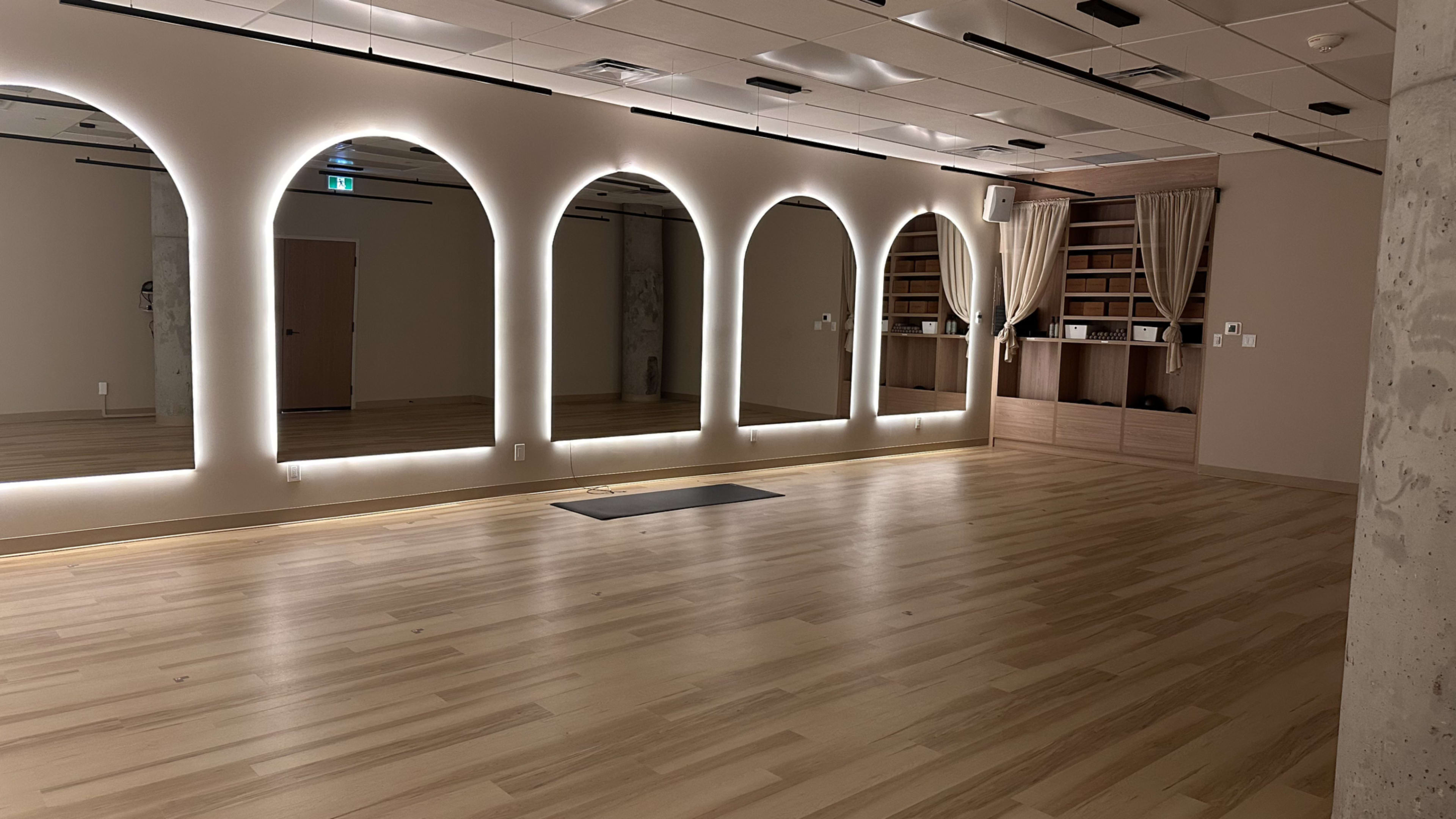 The room features a wooden floor, arched lighted mirrors on one wall, and a neatly organized shelf area at the far end.