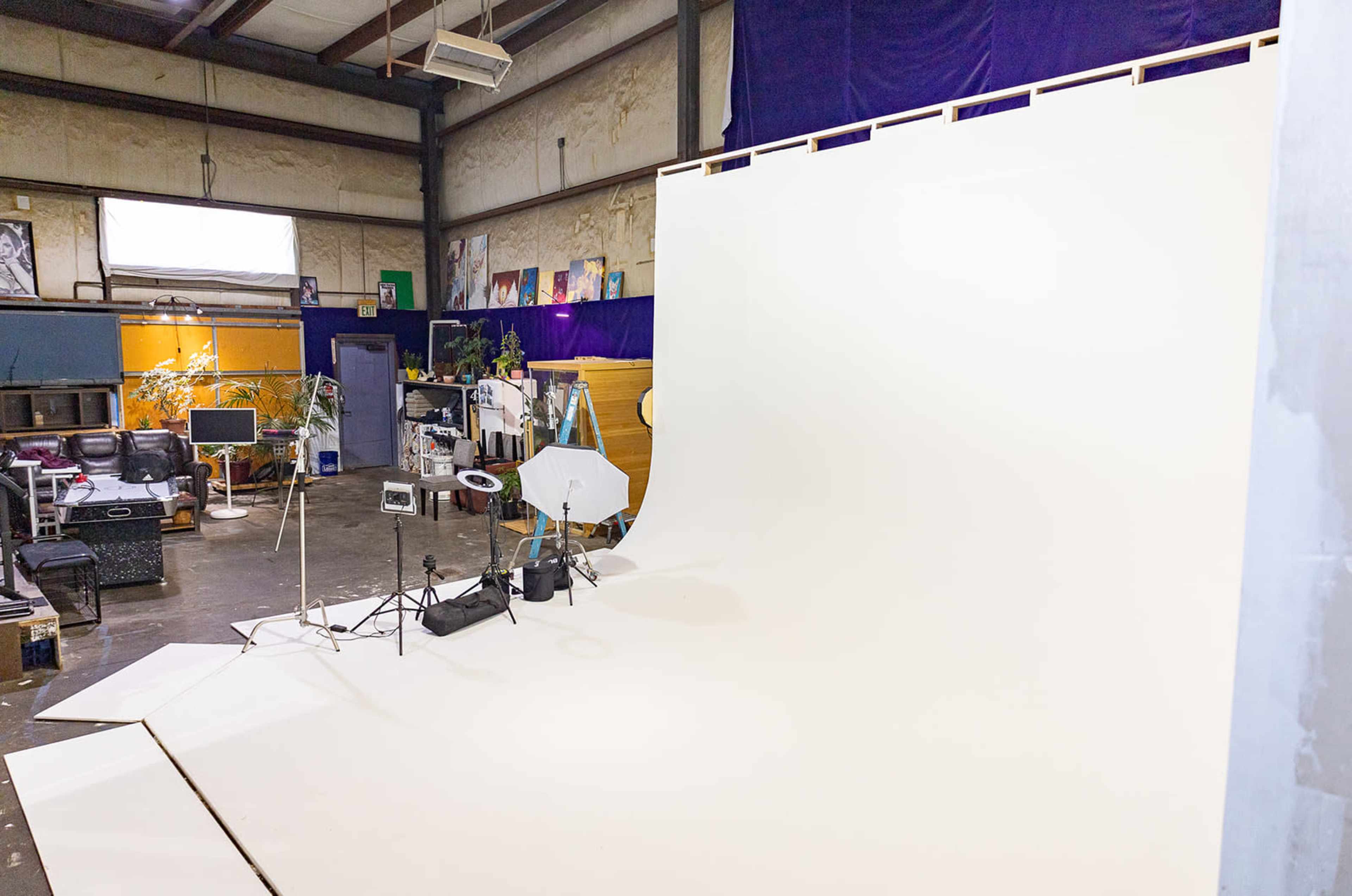 The image shows a photography studio with a large white backdrop, equipment set up, and dim lighting.