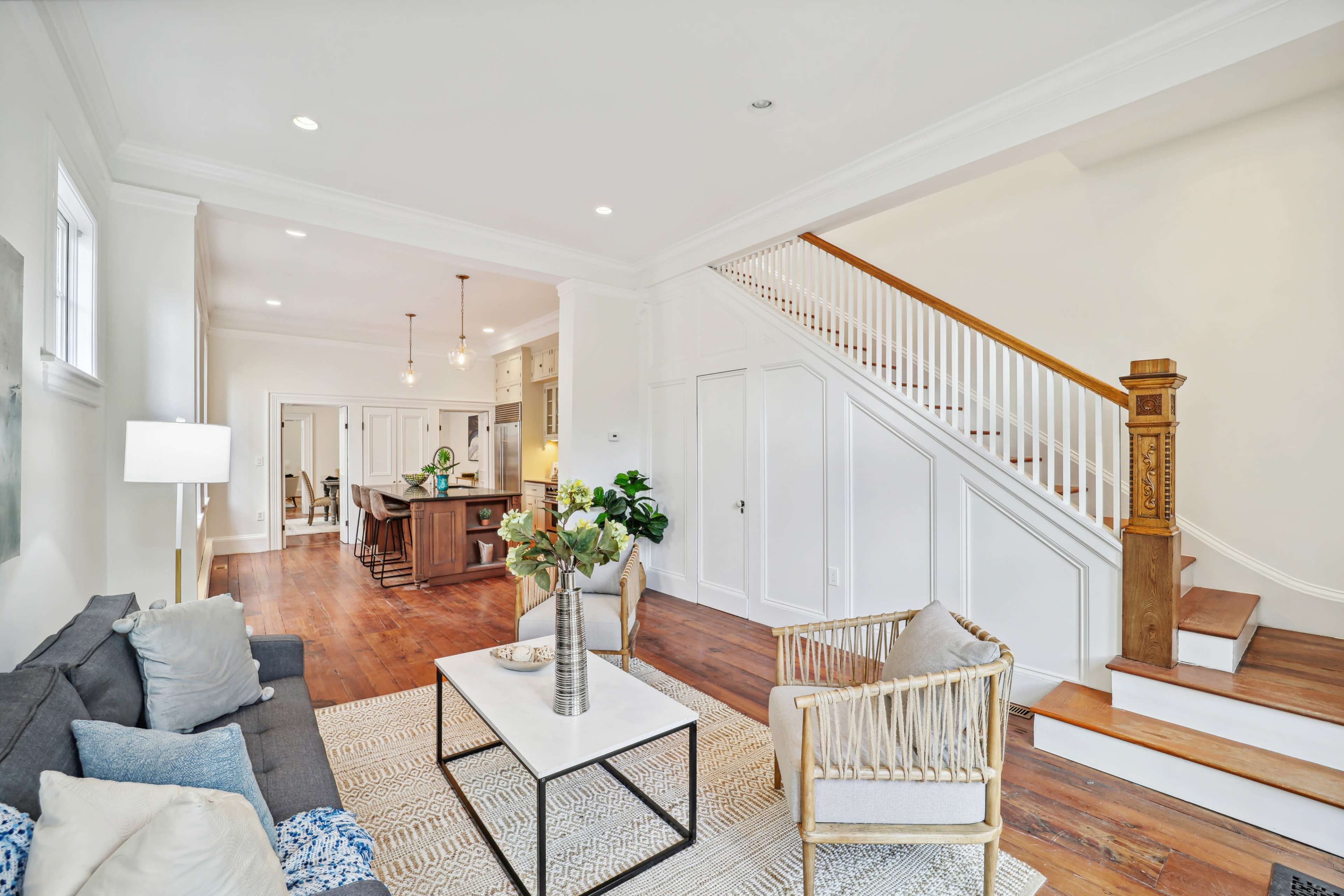 The living room features a gray sofa and a patterned area rug, leading to a staircase and an open kitchen space in the background.