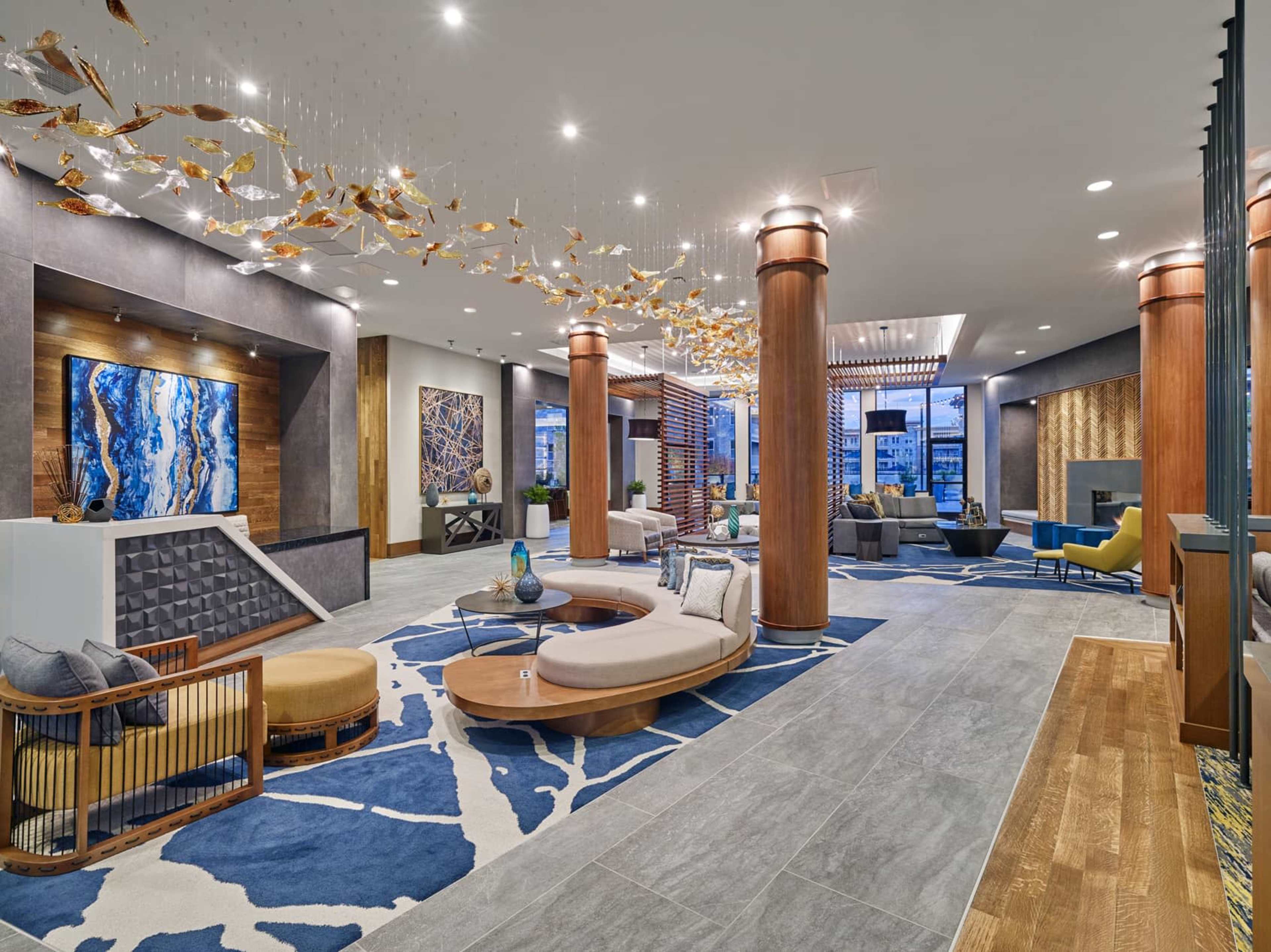 A spacious modern lounge features stylish seating, artistic decor, and a colorful area rug.