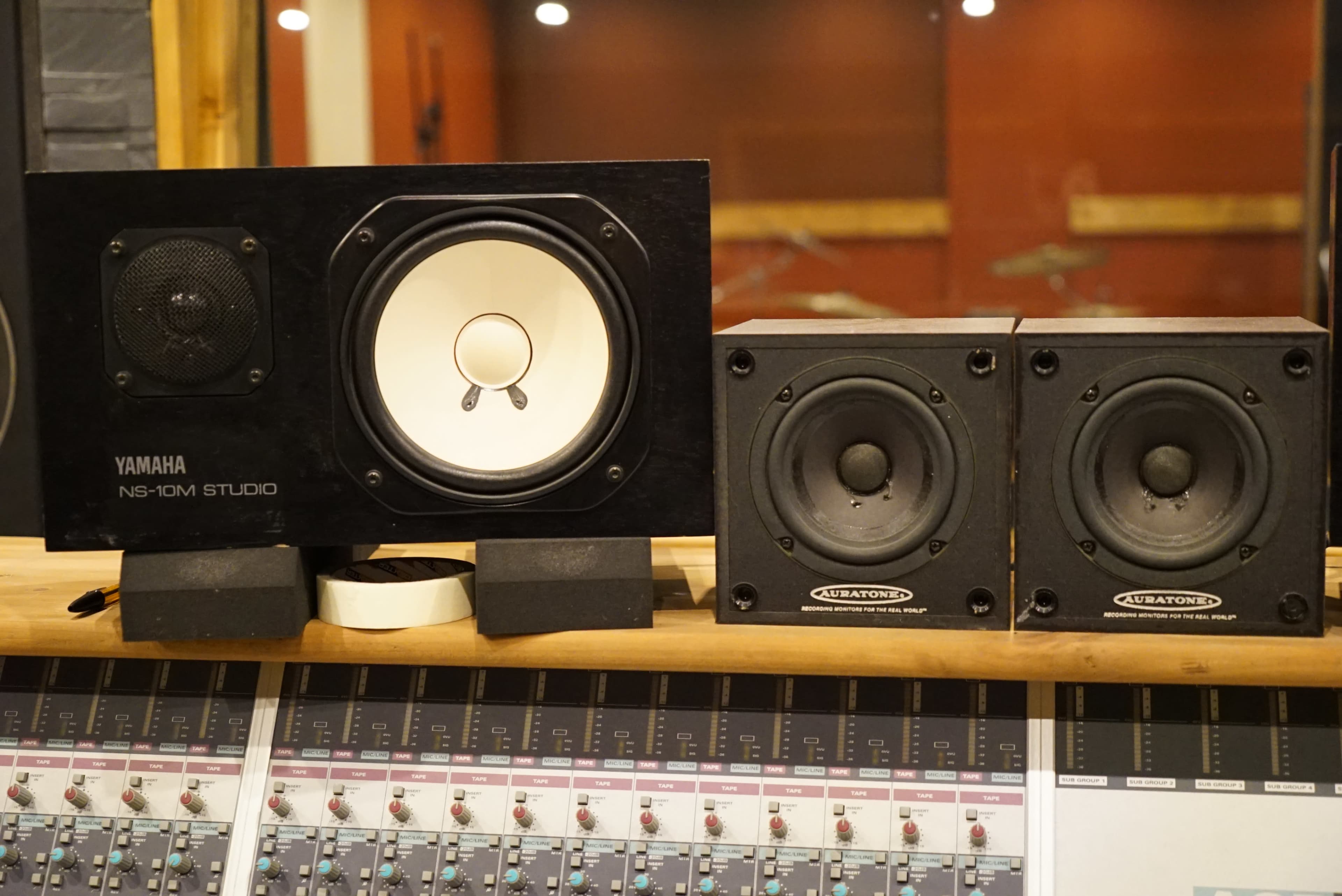 A set of Yamaha NS-10M studio speakers alongside two smaller audio speakers on a wooden surface, with a mixing console in the foreground.