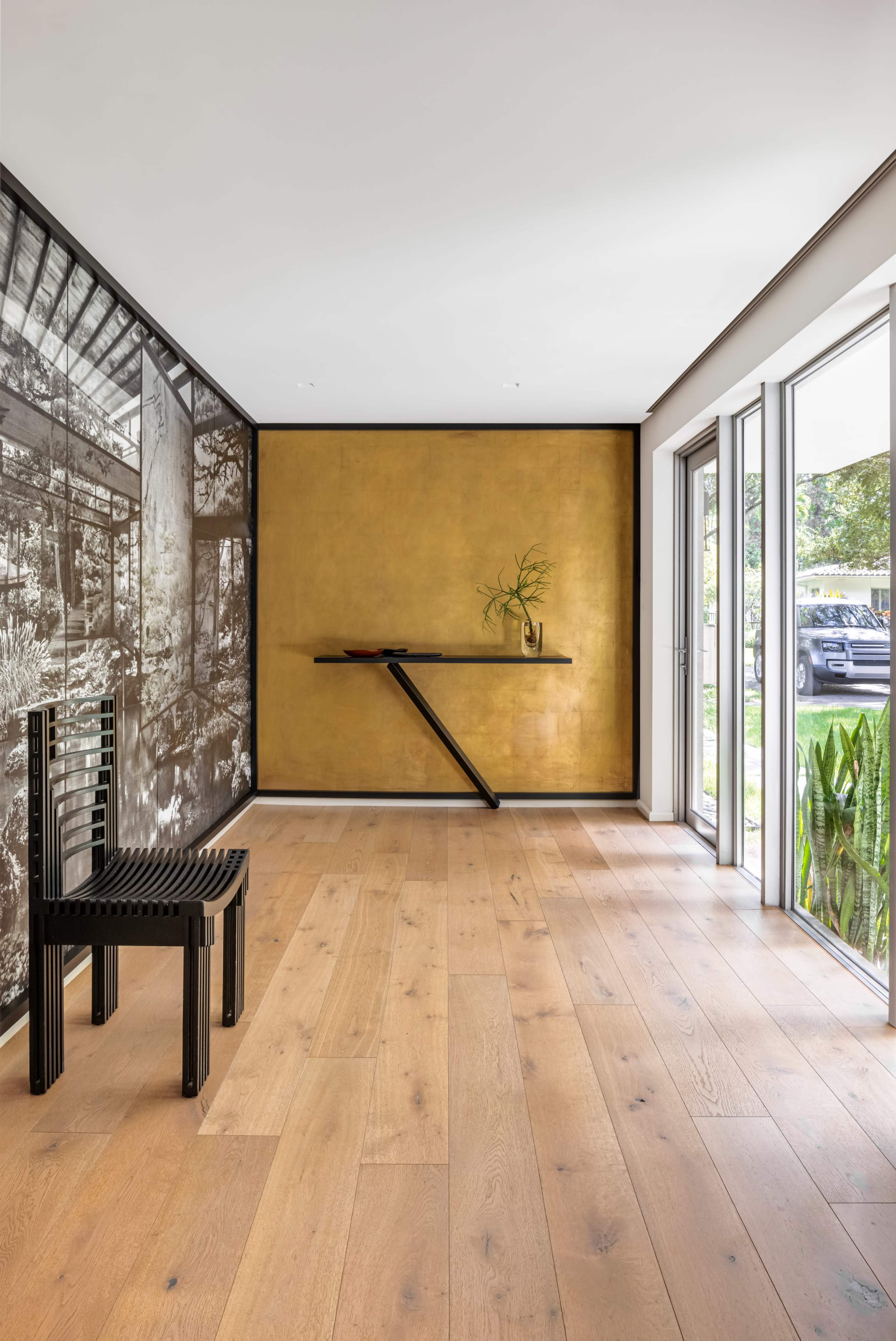 The room features a wooden floor, a black and white decorative wall, a gold-painted wall, a modern wall-mounted shelf, and a black chair.