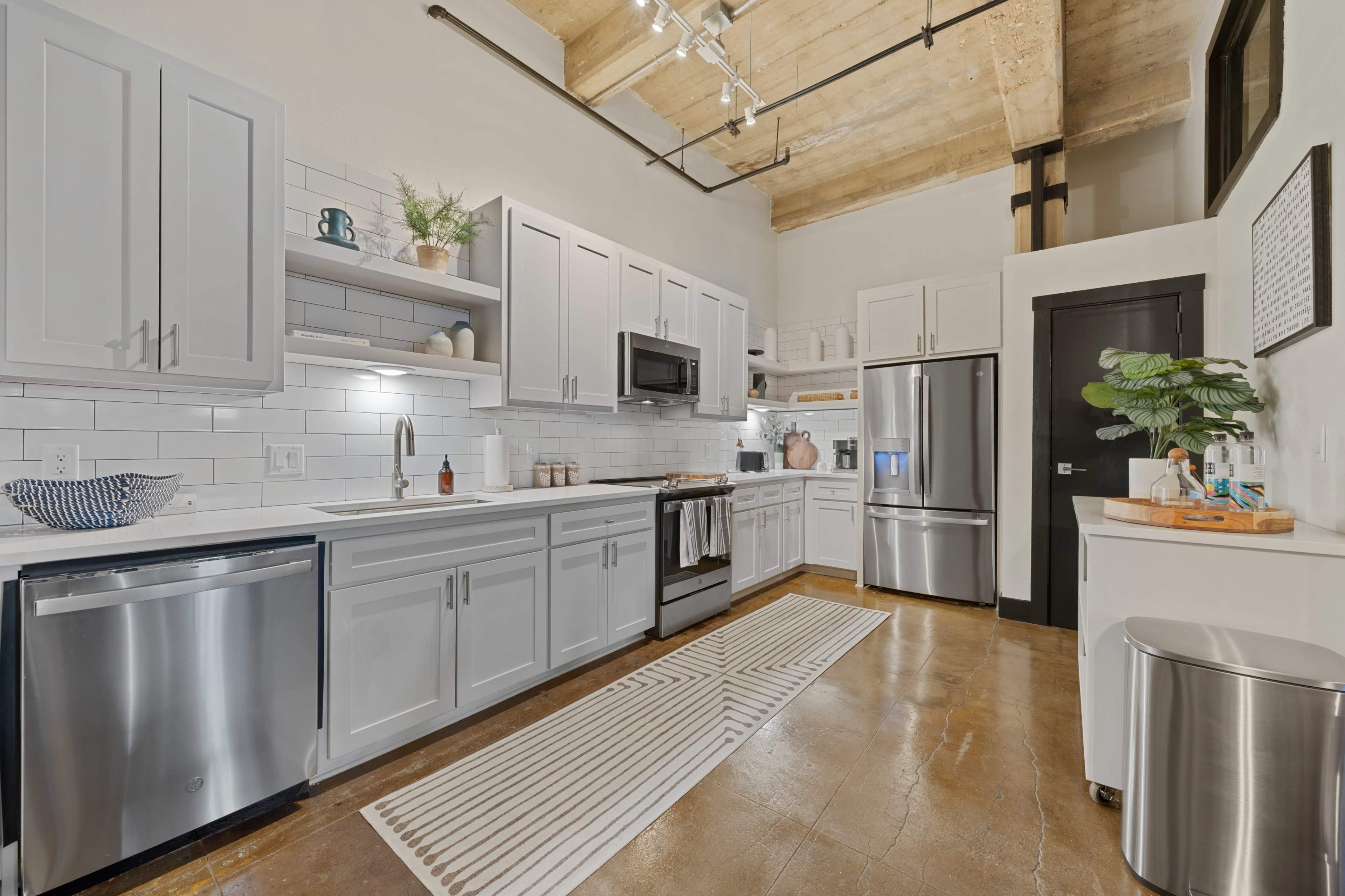 A modern kitchen features white cabinetry, stainless steel appliances, and an island with a decorative bowl, set against a backdrop of exposed wood beams.