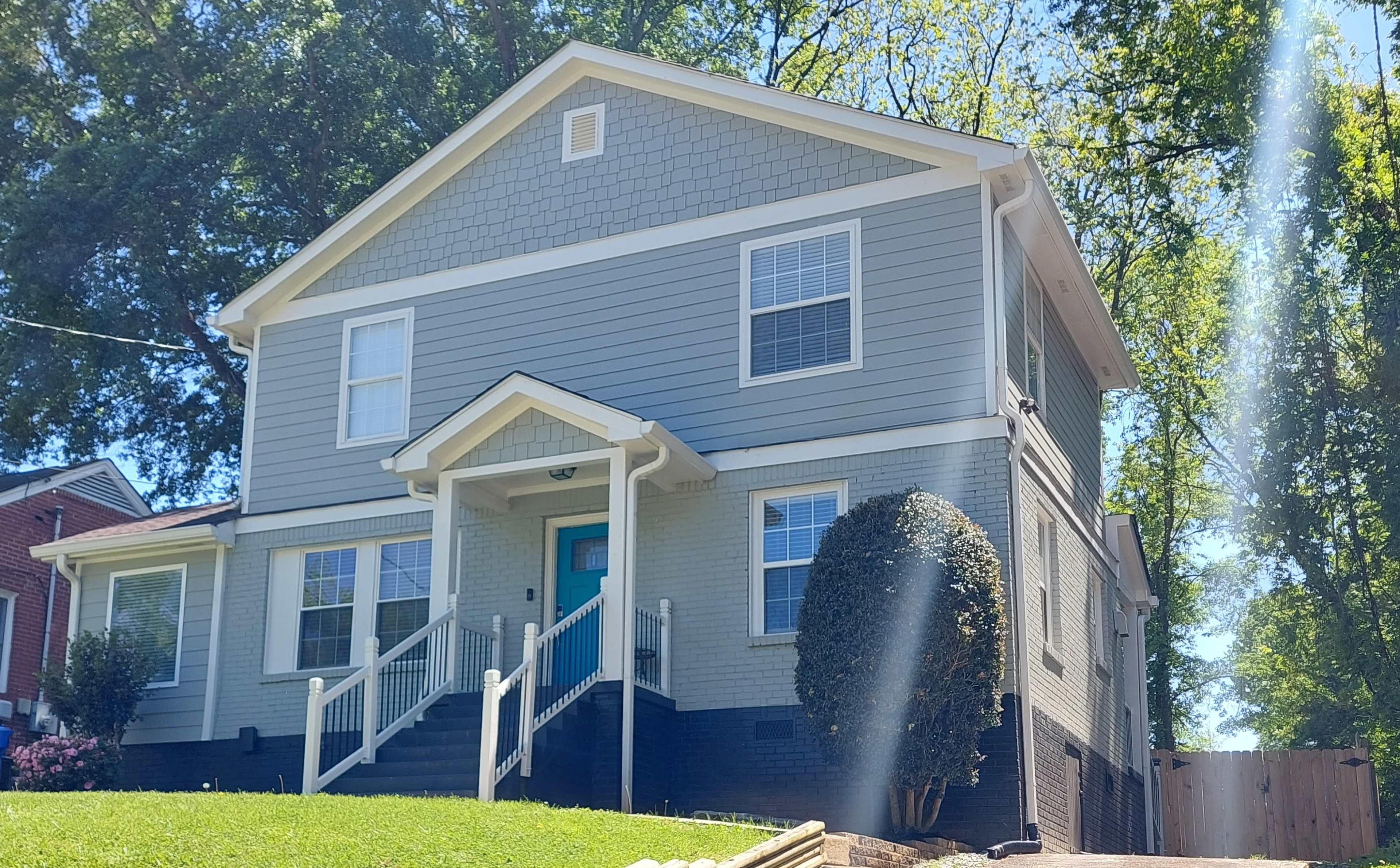 A two-story gray house with white trim, a teal front door, and a lawn that is well-maintained.