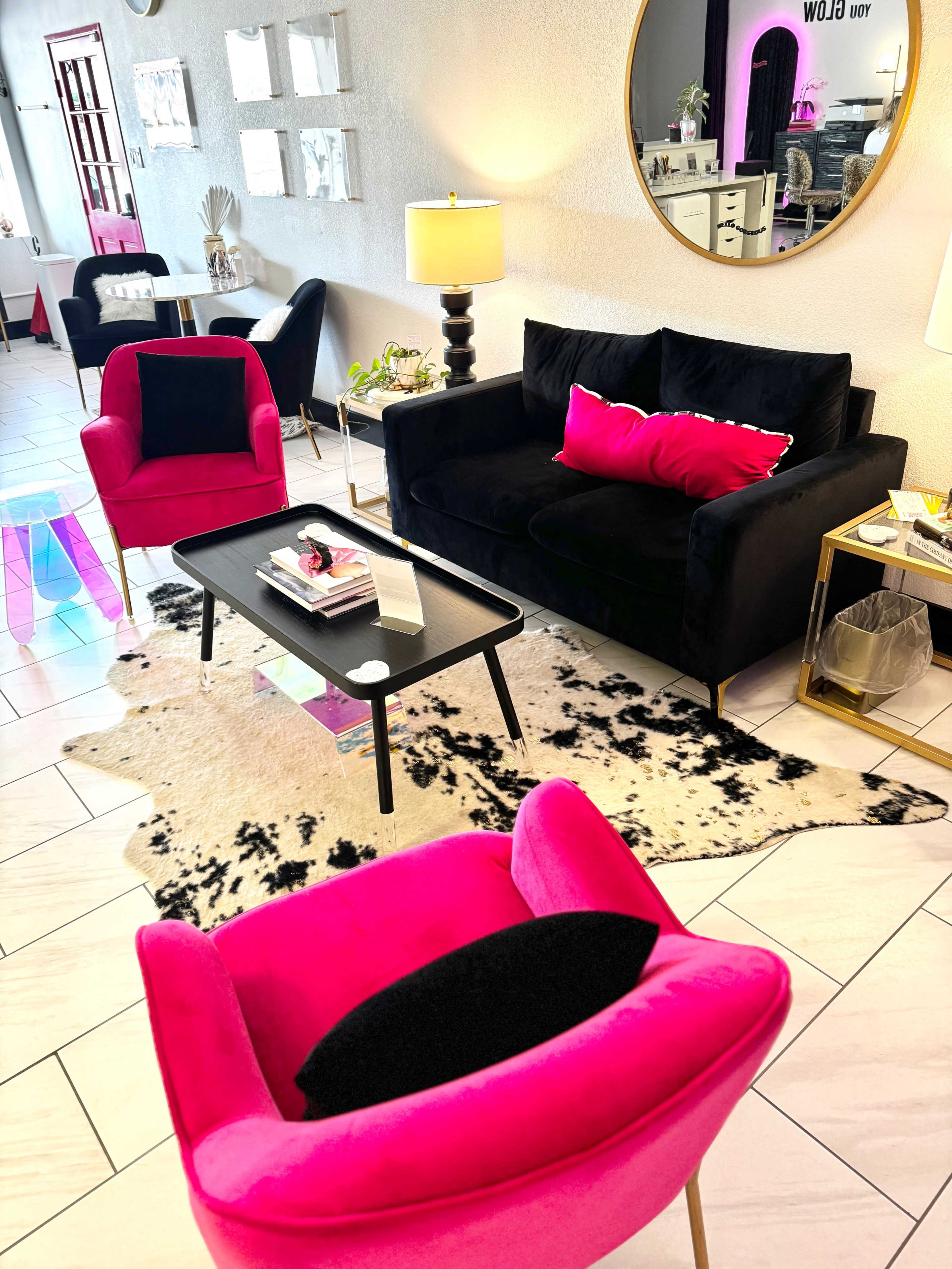 A stylish living room with a black sofa, pink accent chairs, a black coffee table, and a cowhide rug on a tiled floor.