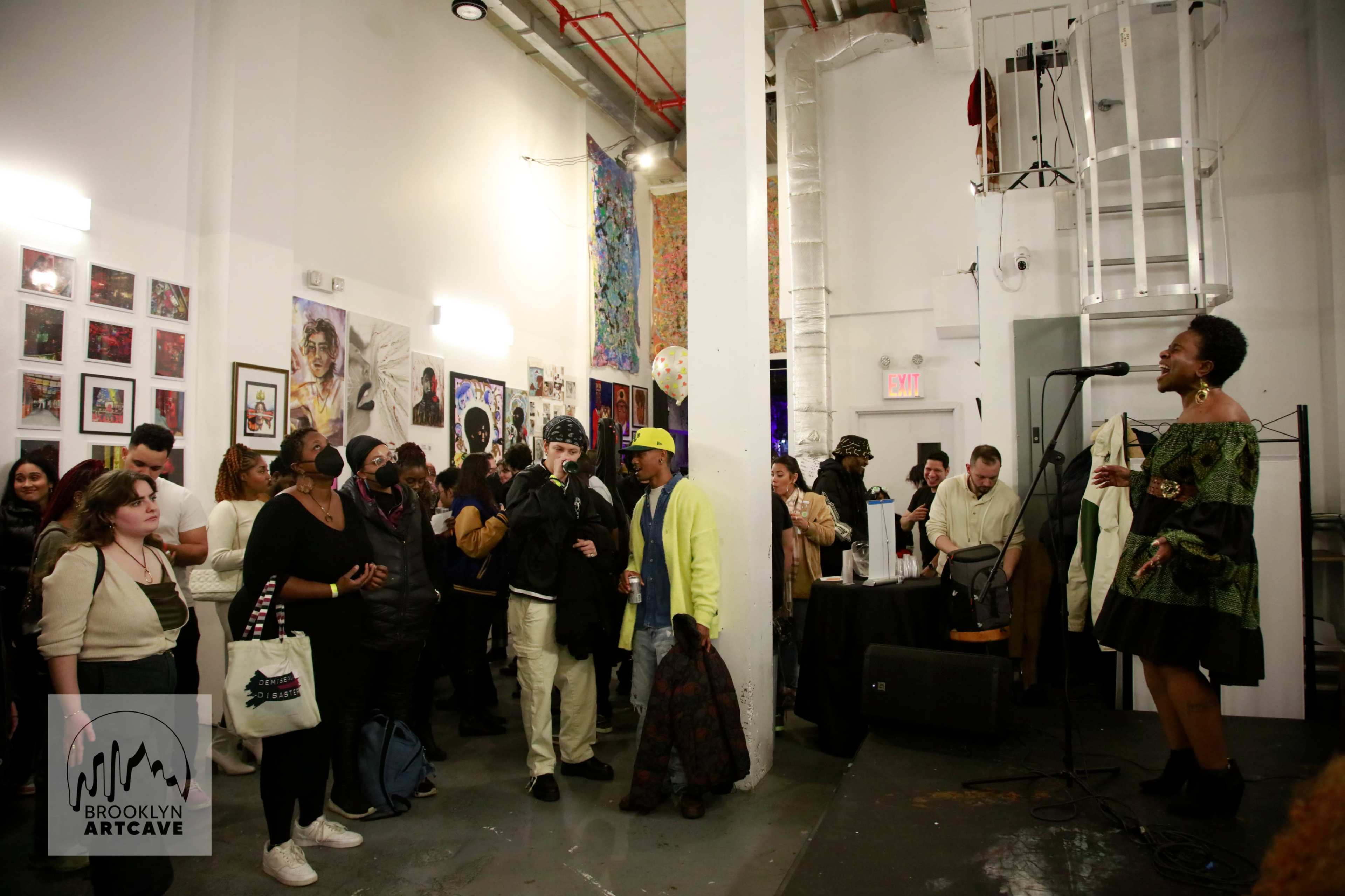 A woman performs on stage in an art gallery filled with an audience engaged in the event.