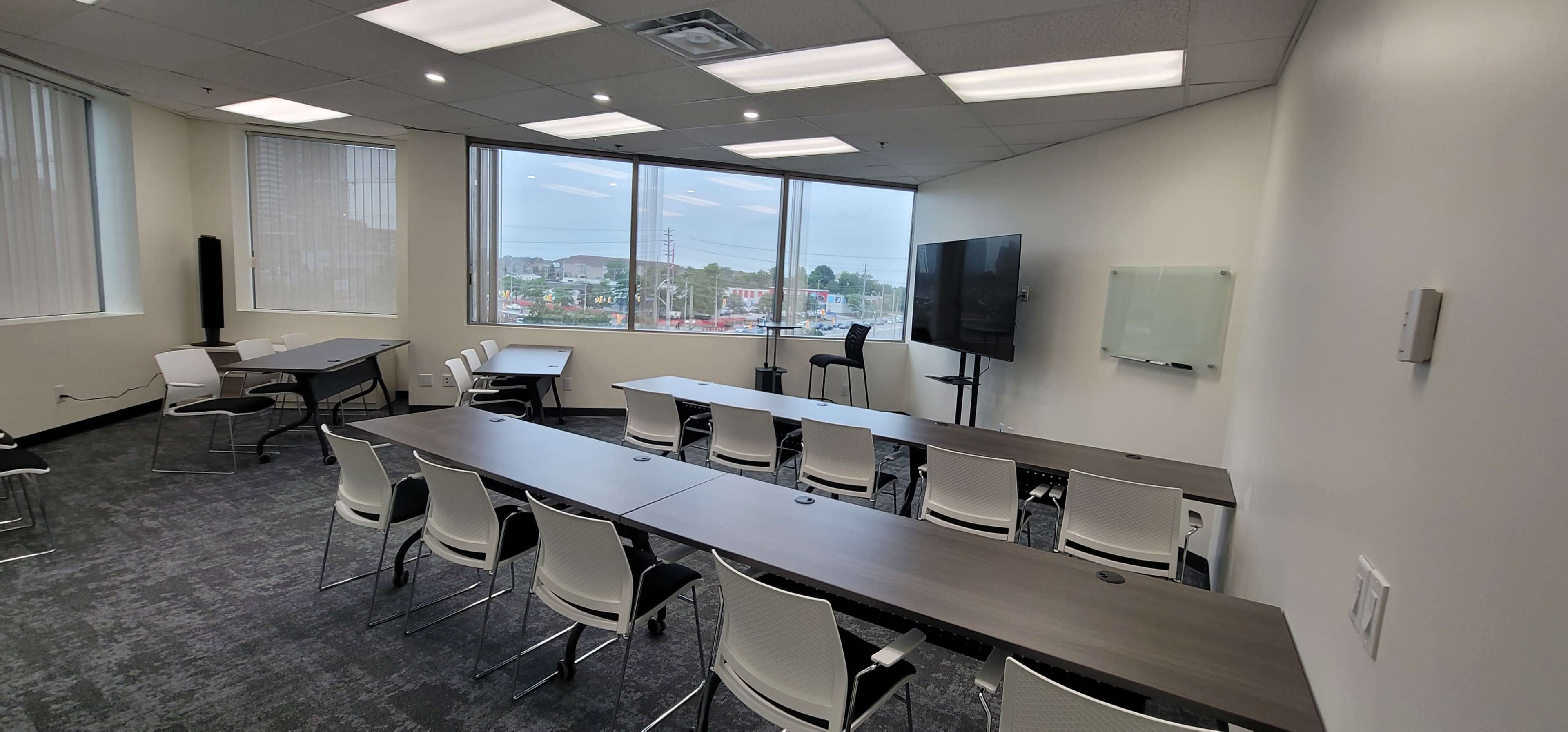 A modern conference room with several tables, chairs, and large windows overlooking an outdoor view.
