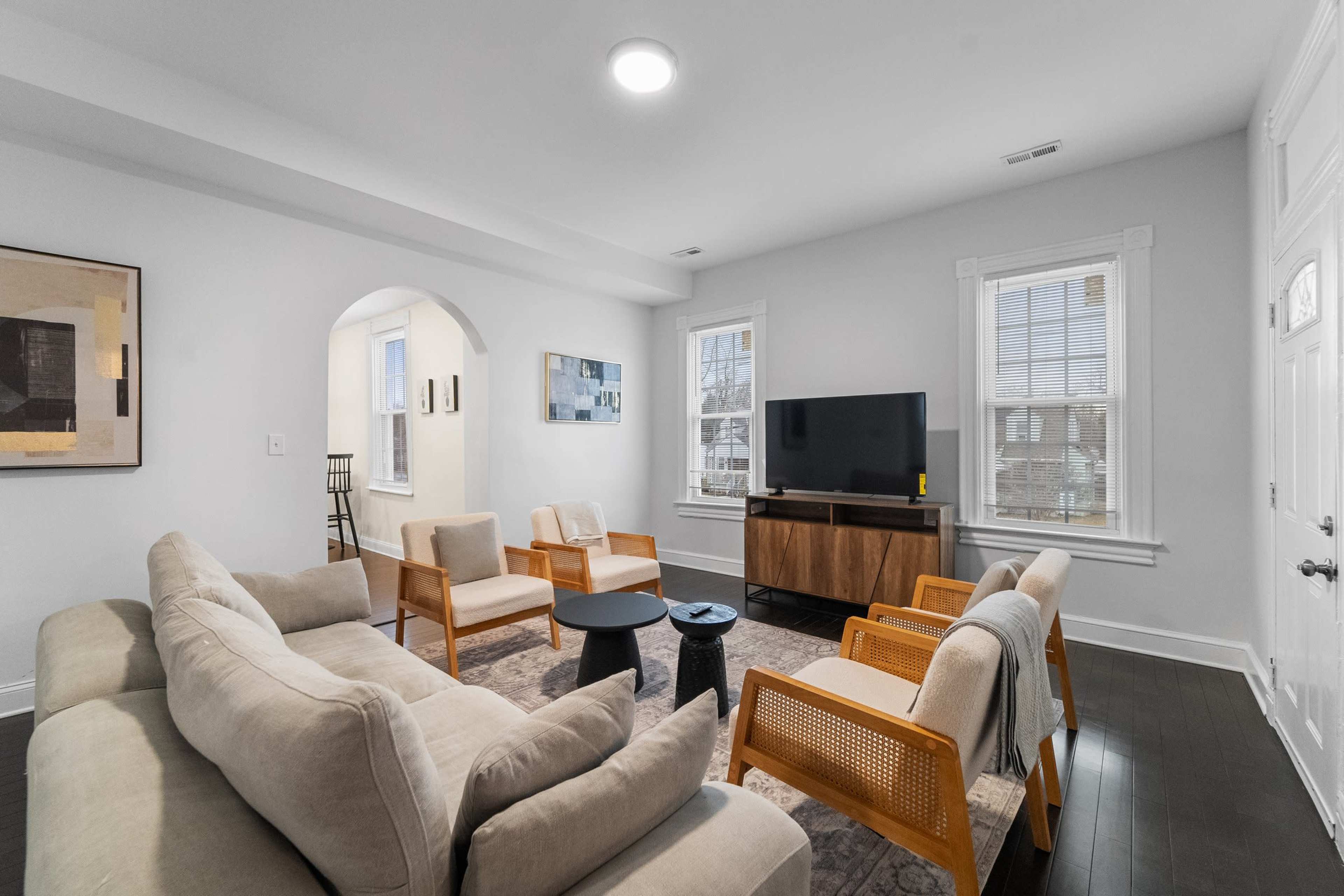The living room features a sectional sofa, armchairs, a coffee table, and a television mounted on a media console, with windows allowing natural light.