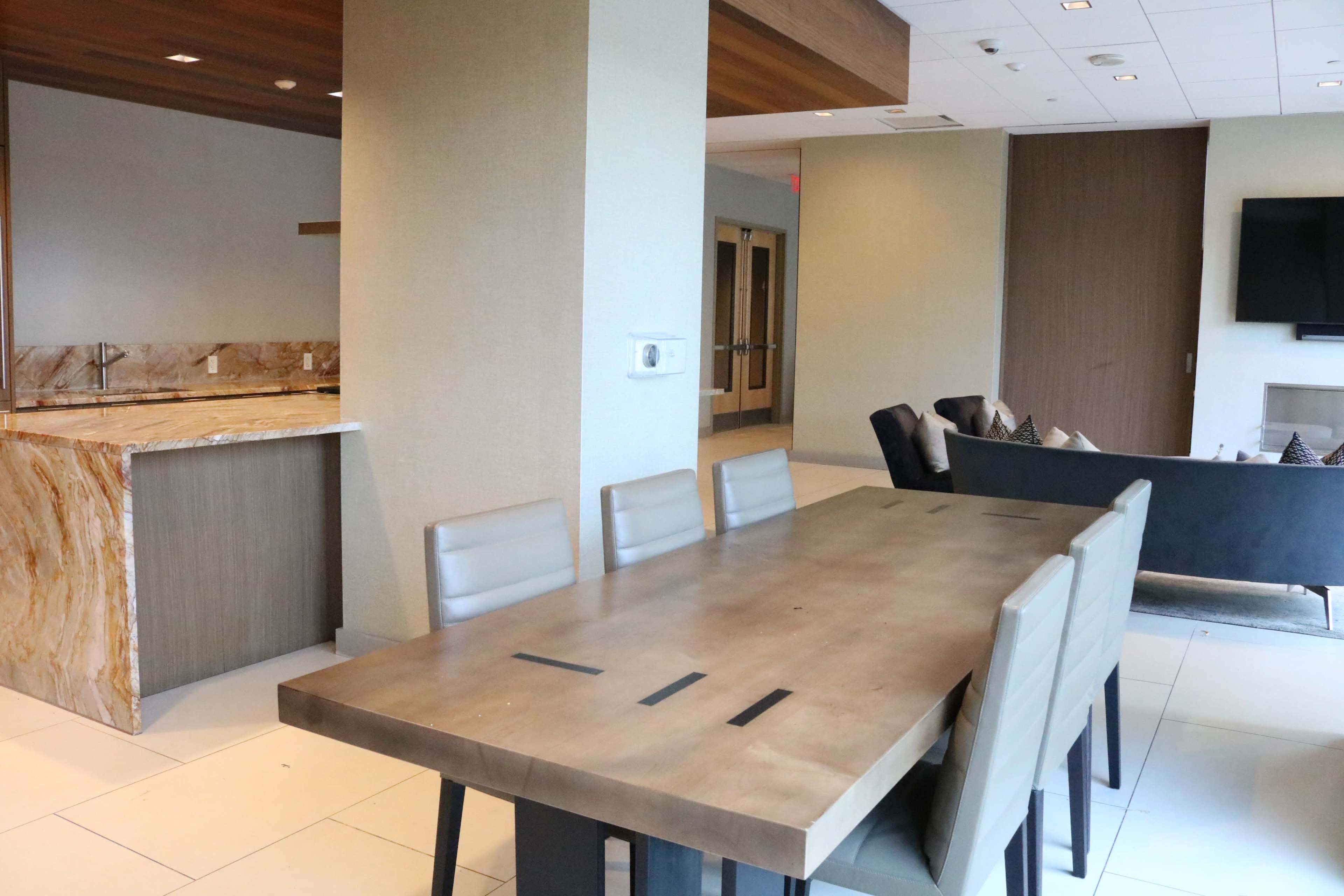 A modern dining area with a long wooden table and a spacious kitchen in the background featuring a marble countertop.