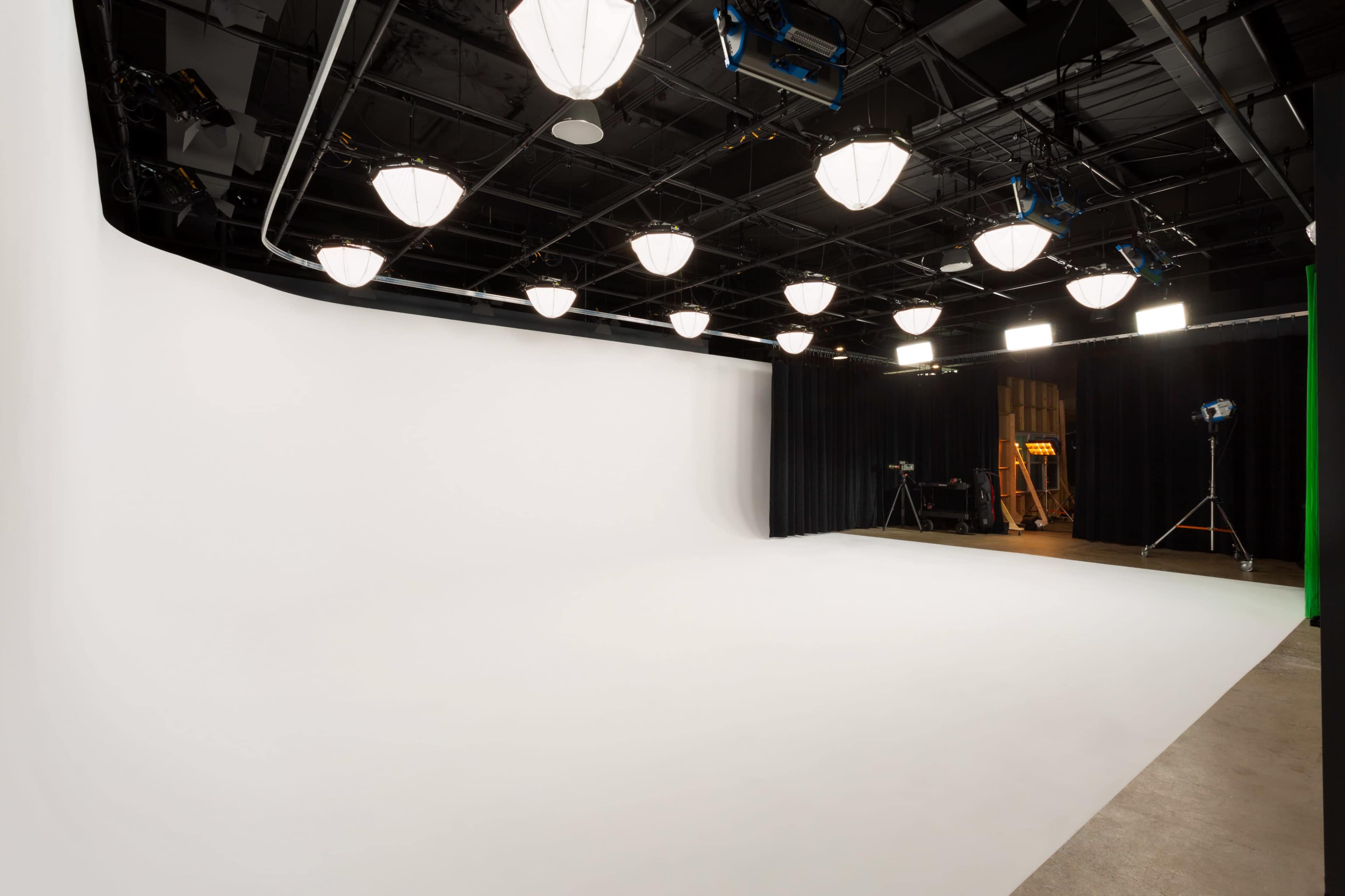 The image shows a spacious photography studio with a white seamless backdrop and overhead lighting fixtures.