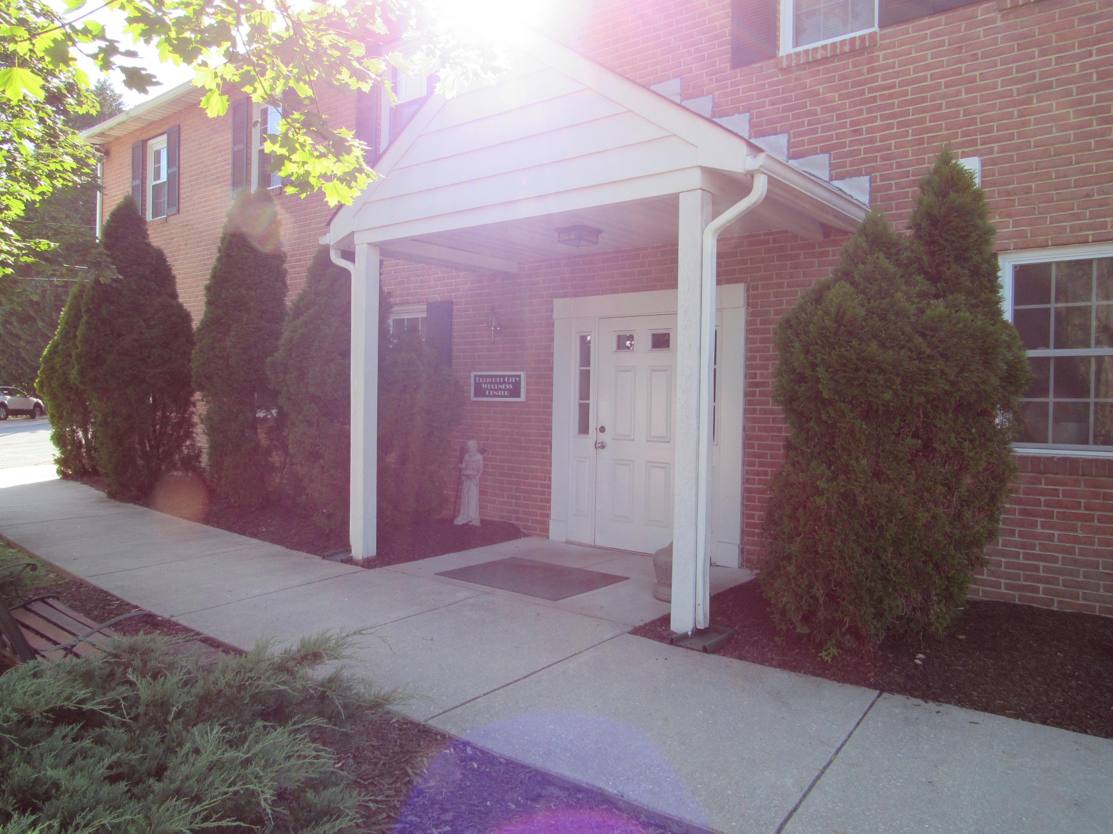 A brick building entrance with a covered porch and neatly trimmed shrubs on either side.