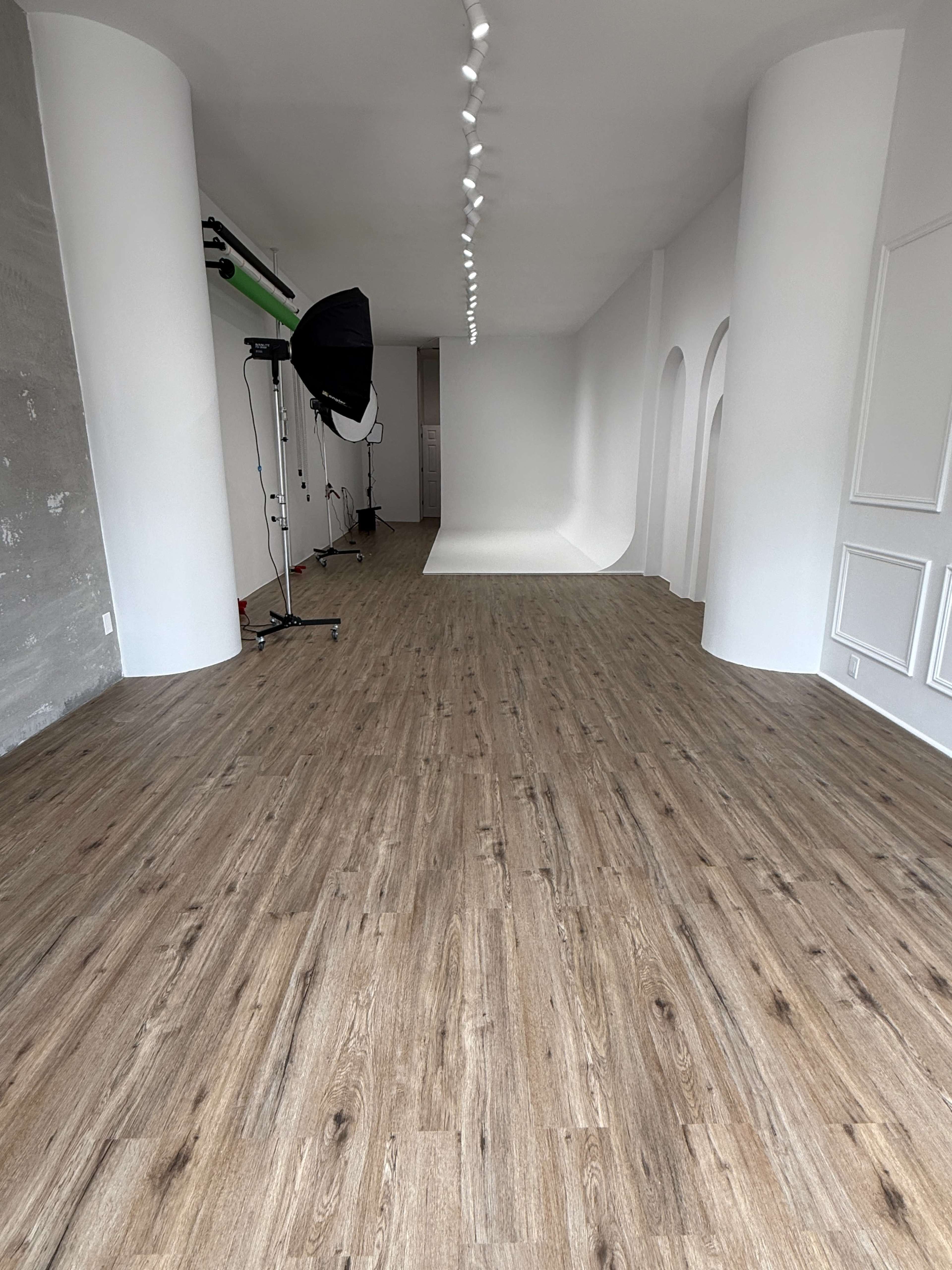 The image shows a spacious studio with wooden flooring, white walls, and a seamless background setup at the far end.
