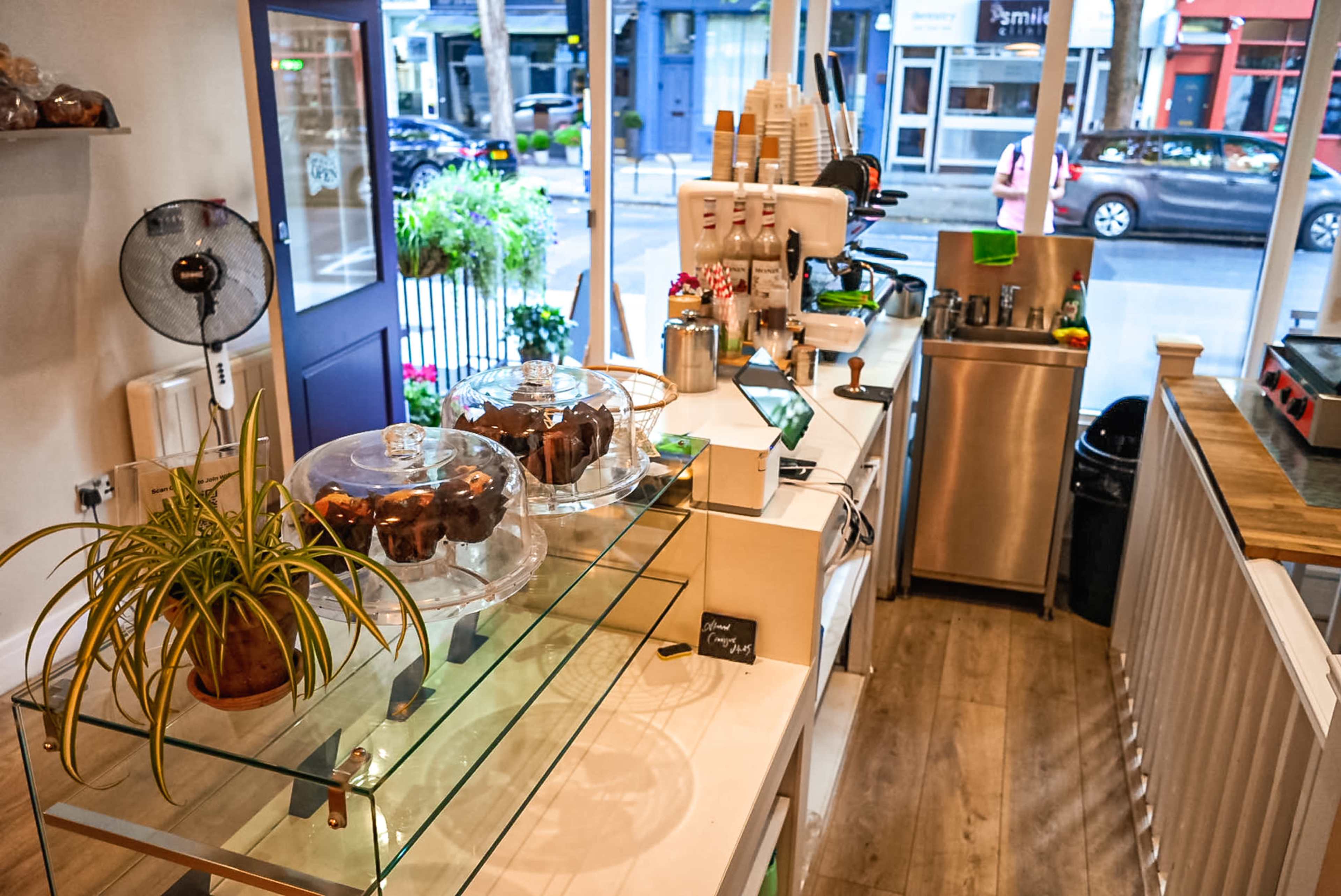 A coffee shop interior with a serving counter displaying baked goods under glass domes, an espresso machine, and a modern decor setup.