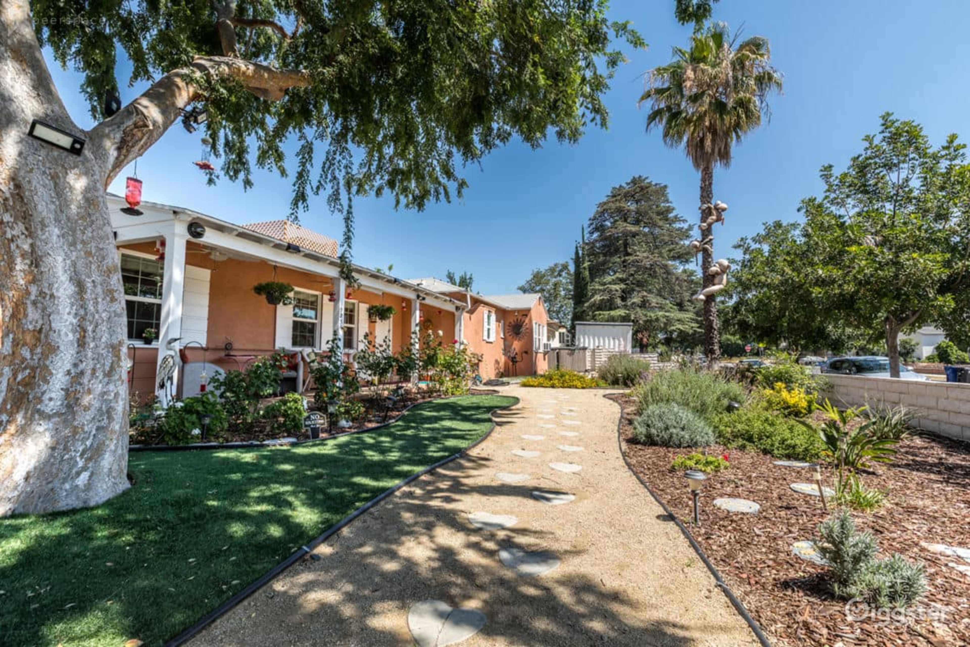 A landscaped pathway with stepping stones leads to a single-story home surrounded by various plants and trees.