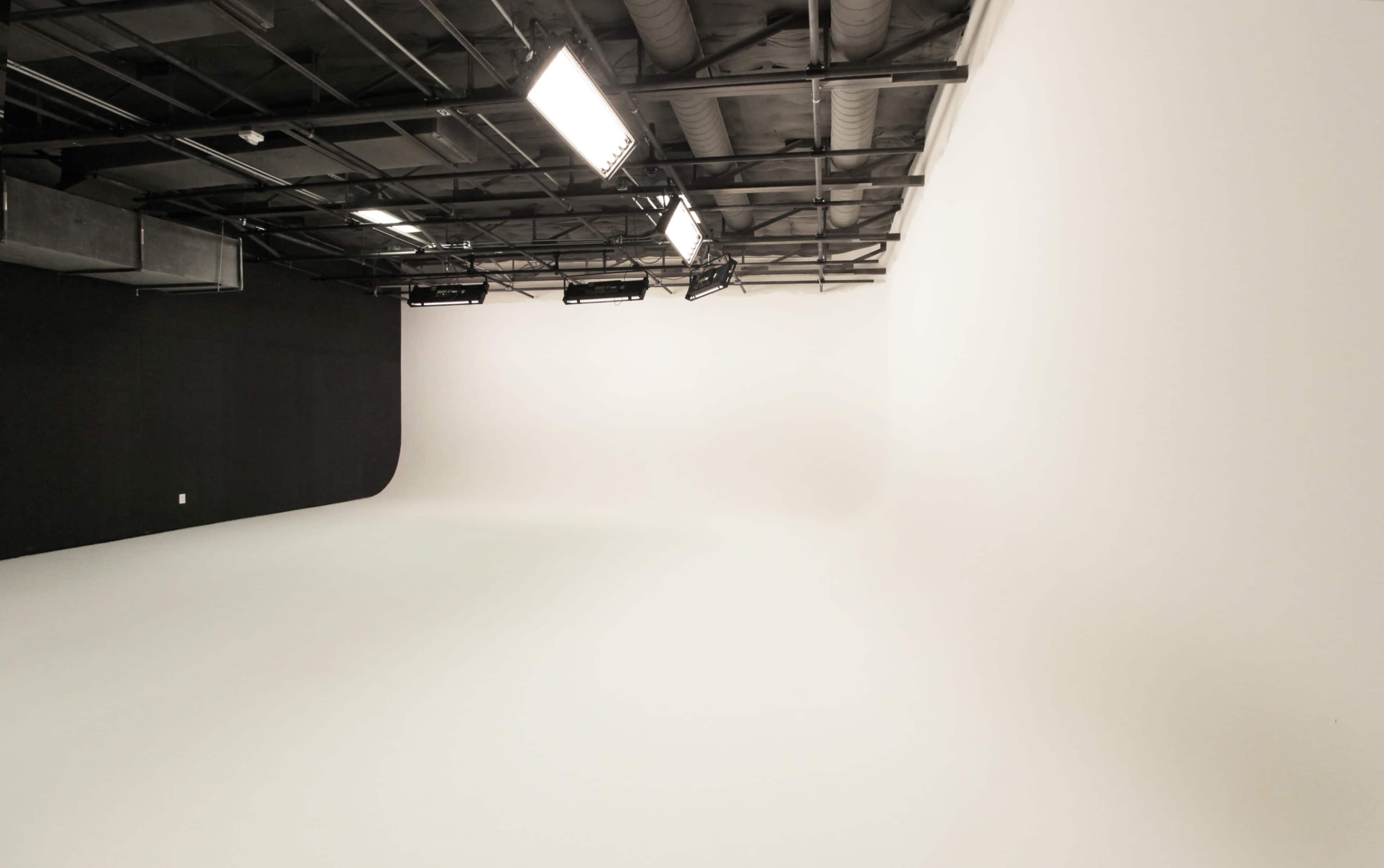 A minimalistic photo studio with a white backdrop and black wall sections, illuminated by overhead lights.
