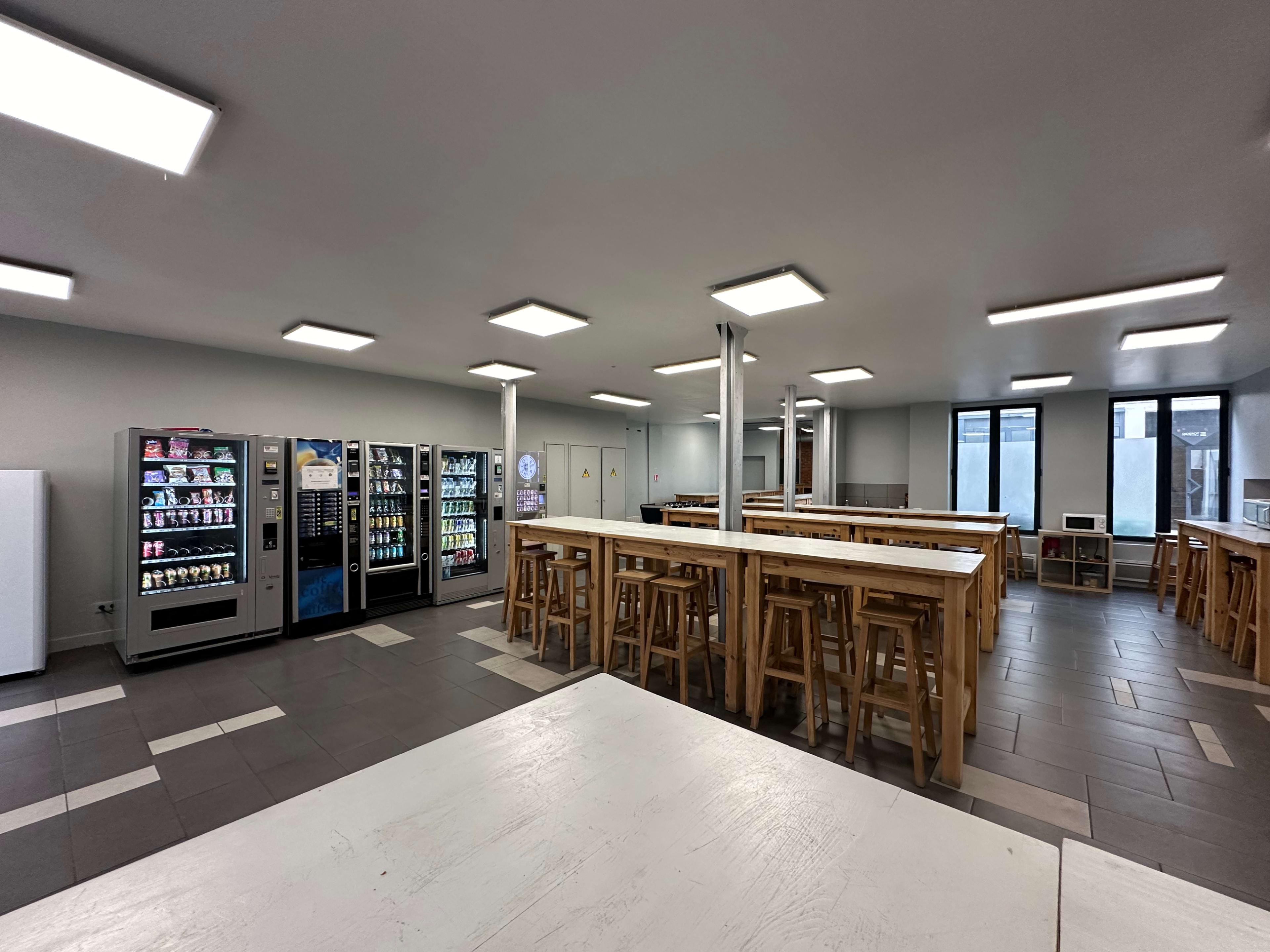 A spacious break room with several vending machines, long tables, and large windows letting in natural light.