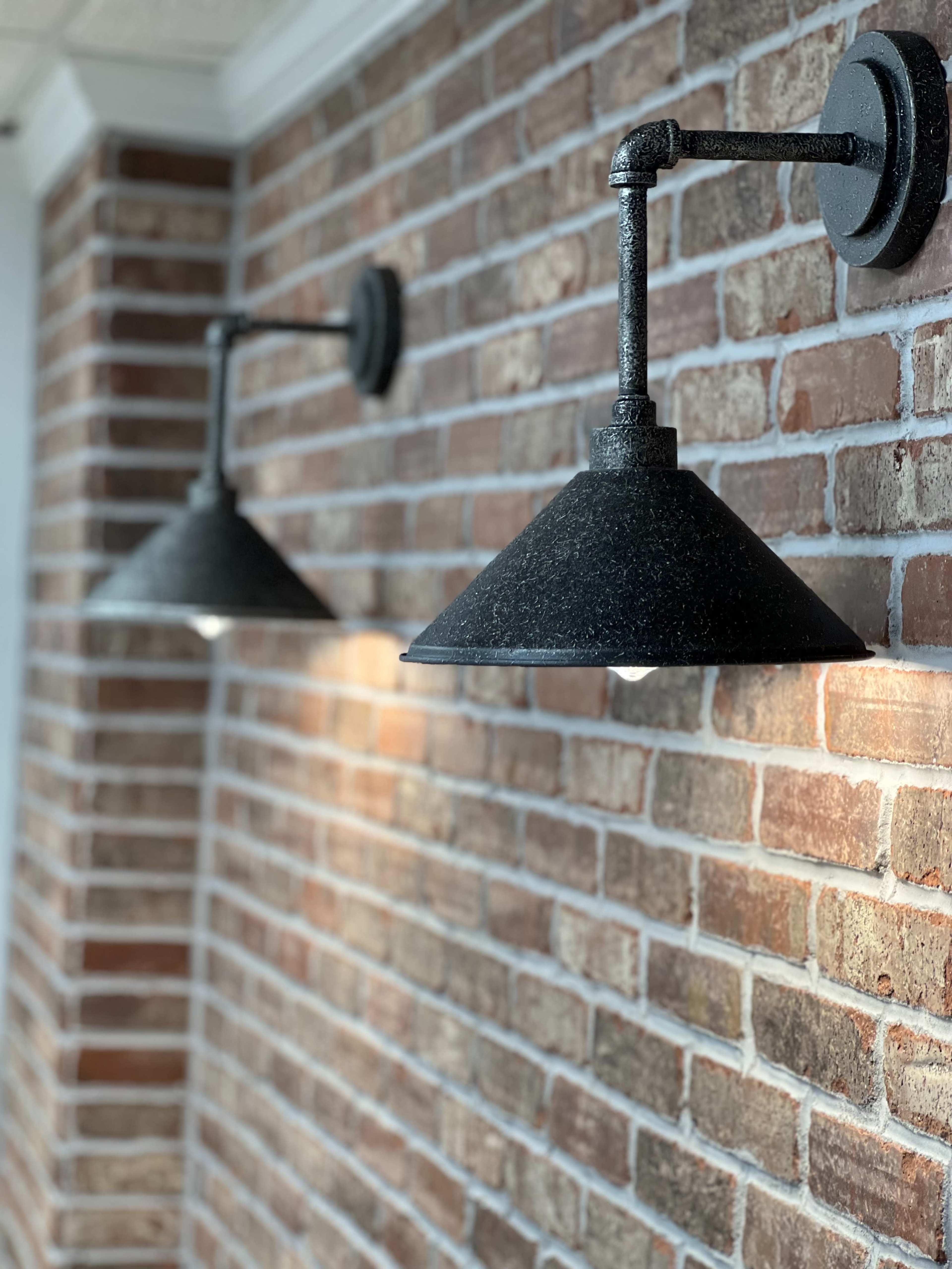 Two industrial-style wall sconces mounted on a red brick wall.