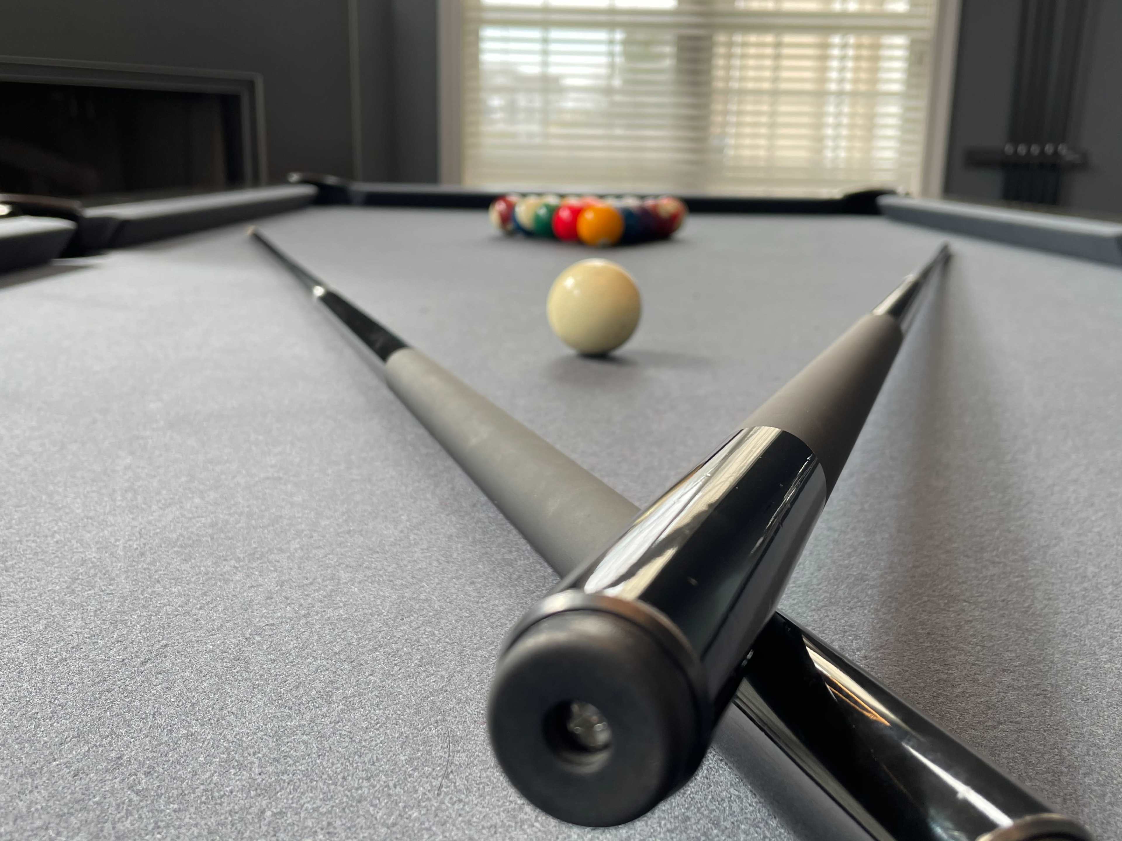 A billiard table with two cues crossed in the foreground and a set of colorful balls arranged in a triangle at the far end.