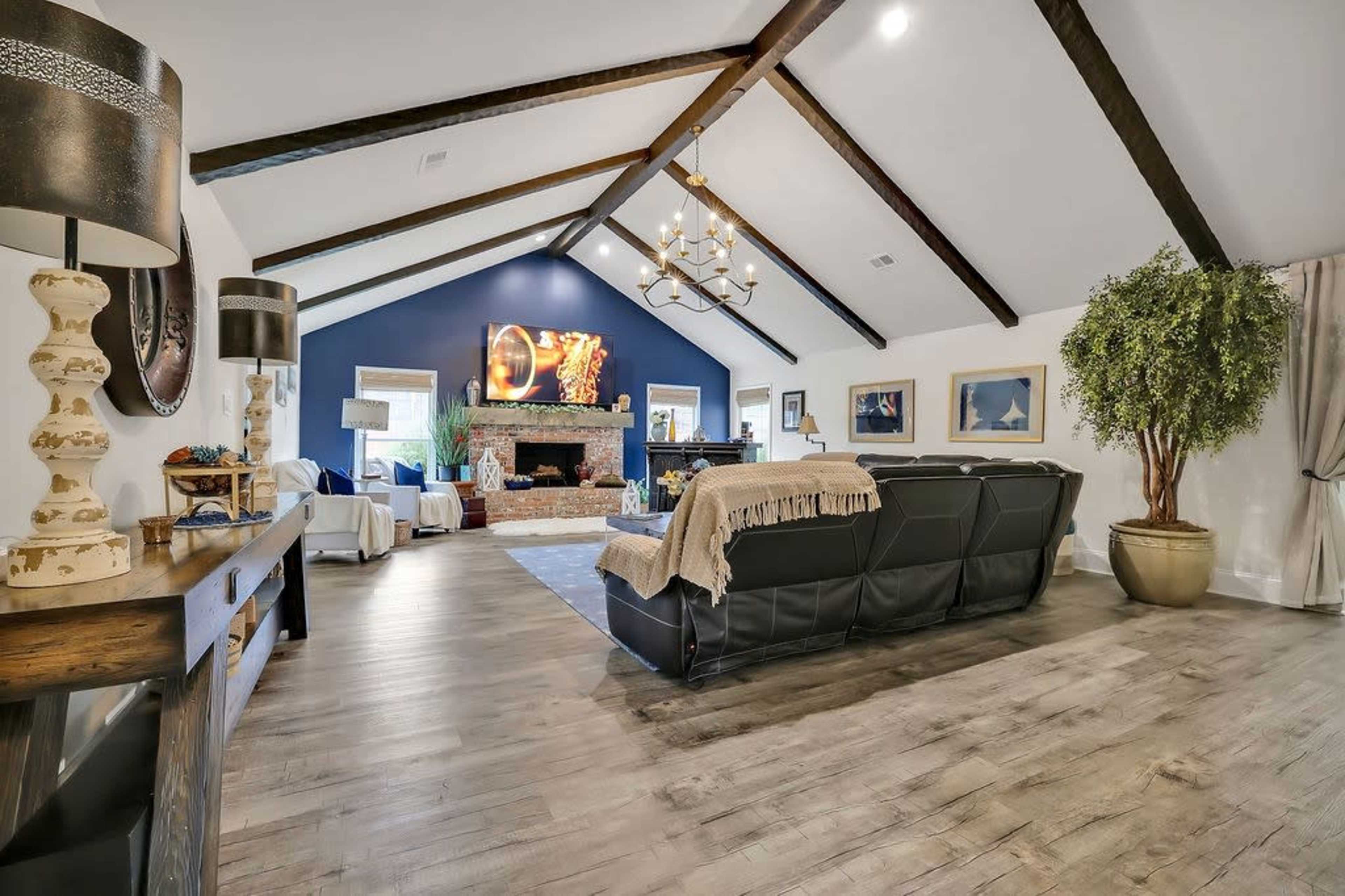 The living room features a high ceiling with exposed beams, a fireplace, and a large television mounted on a blue accent wall.